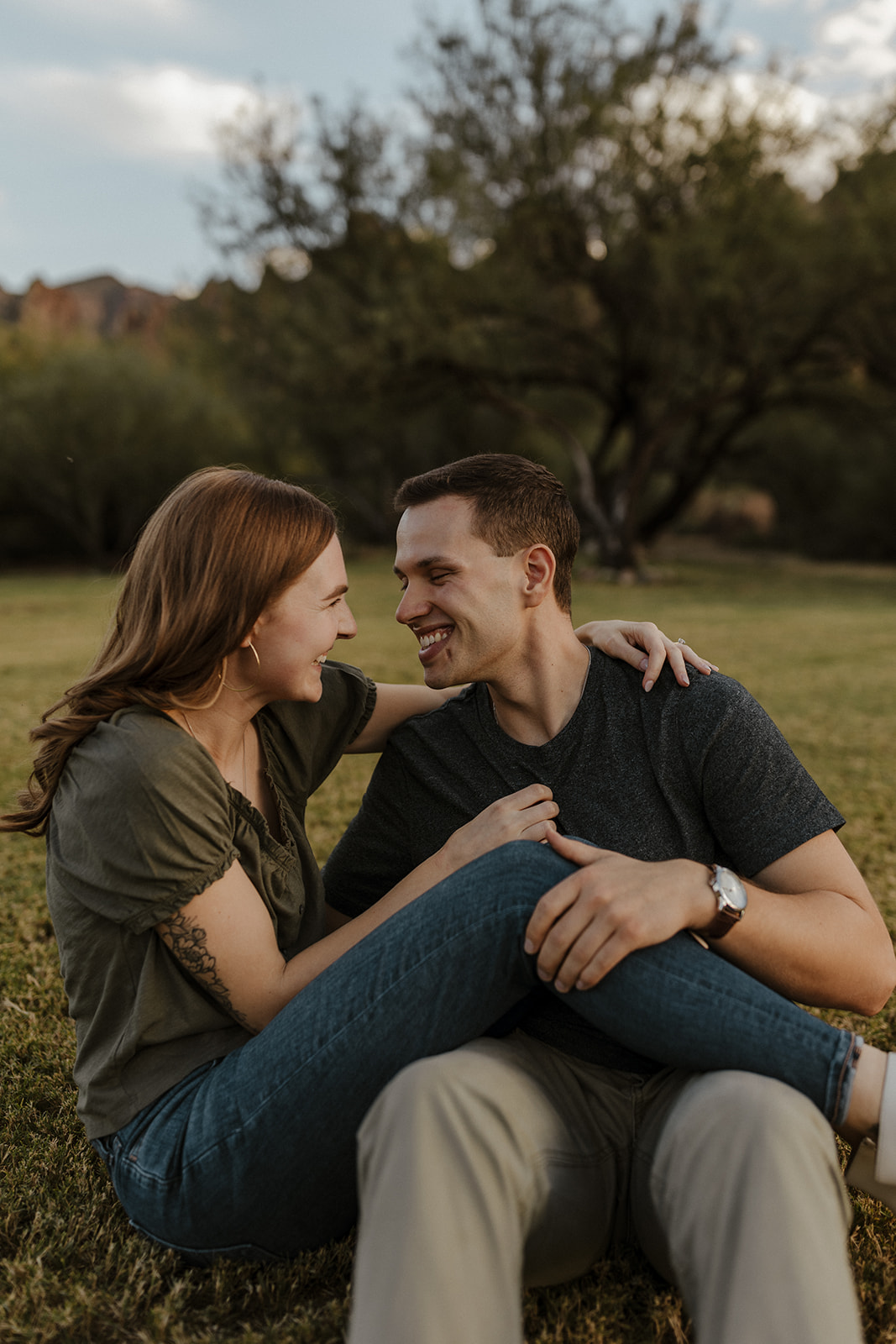newly engaged couple sitting on the grass holding each other 