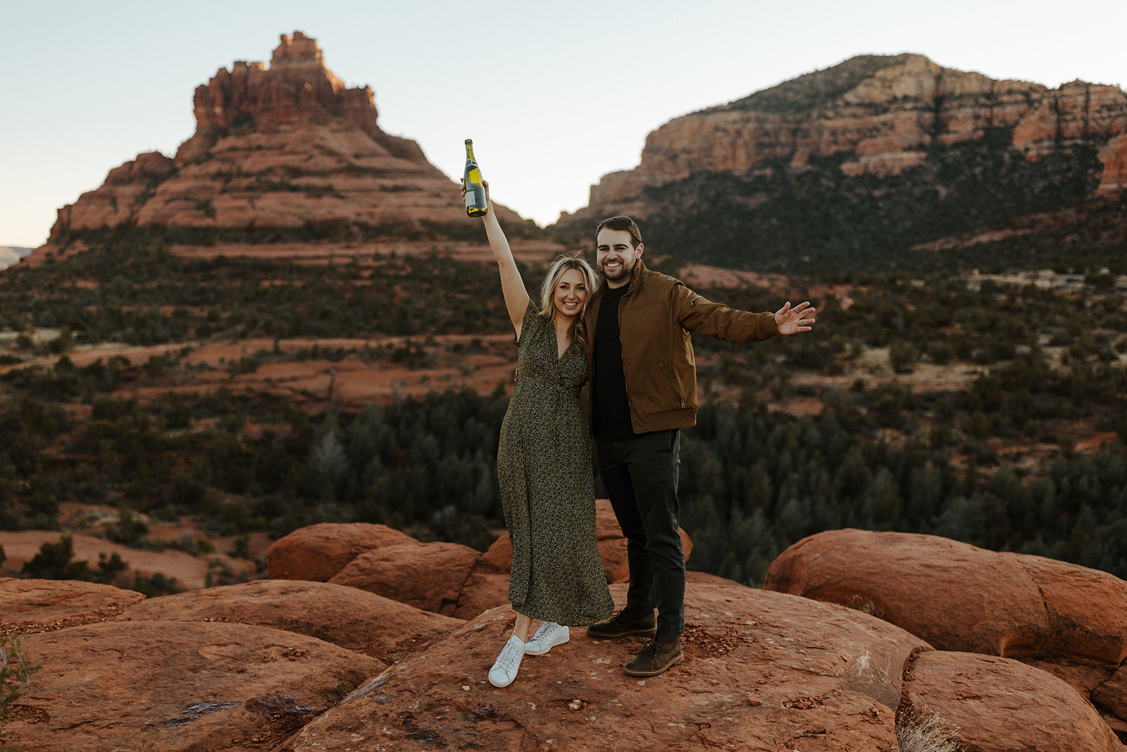 couple holding up champagne during sedona engagement photos