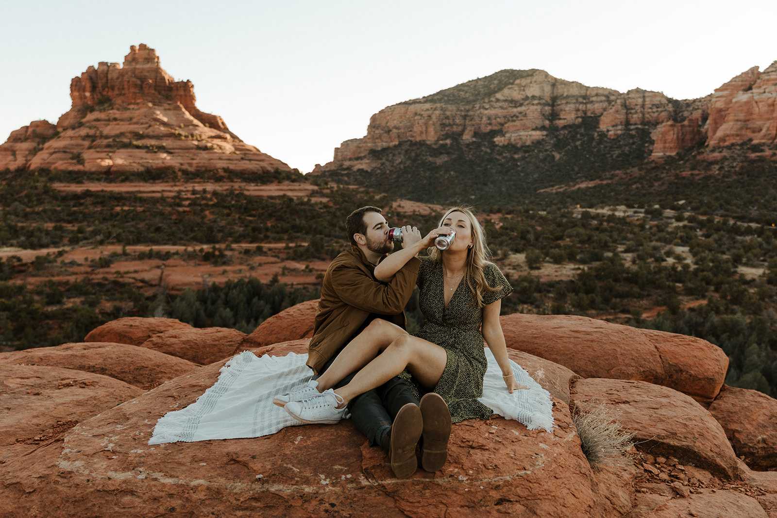 engaged couple sitting on a blanket on the red rocks drinking a beer