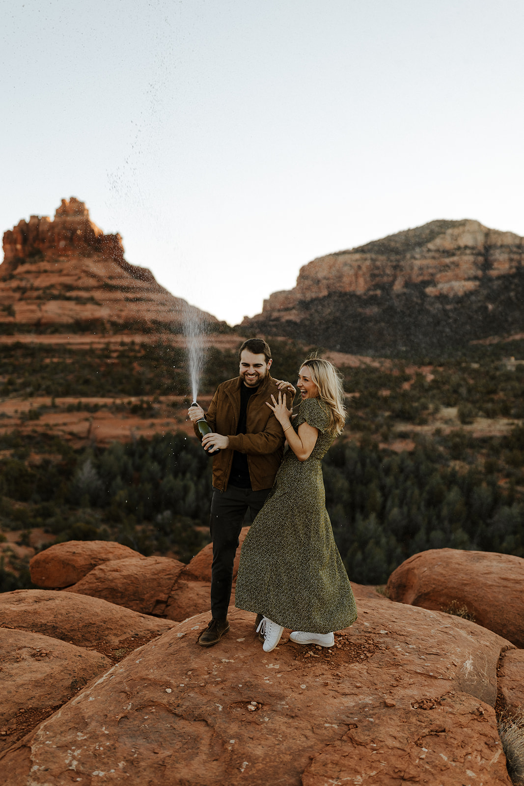 engaged couple popping champagne on top of a mountain in sedona