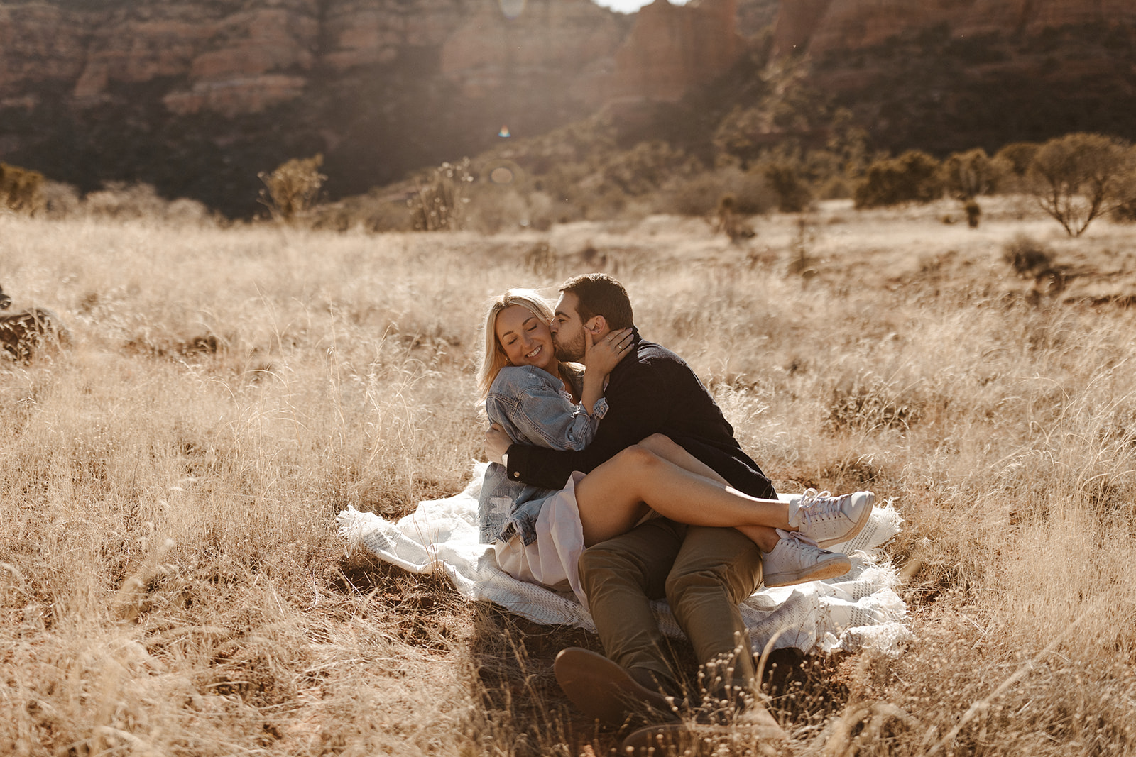 engaged couple sitting on a blanket in the grass during sedona engagement photos