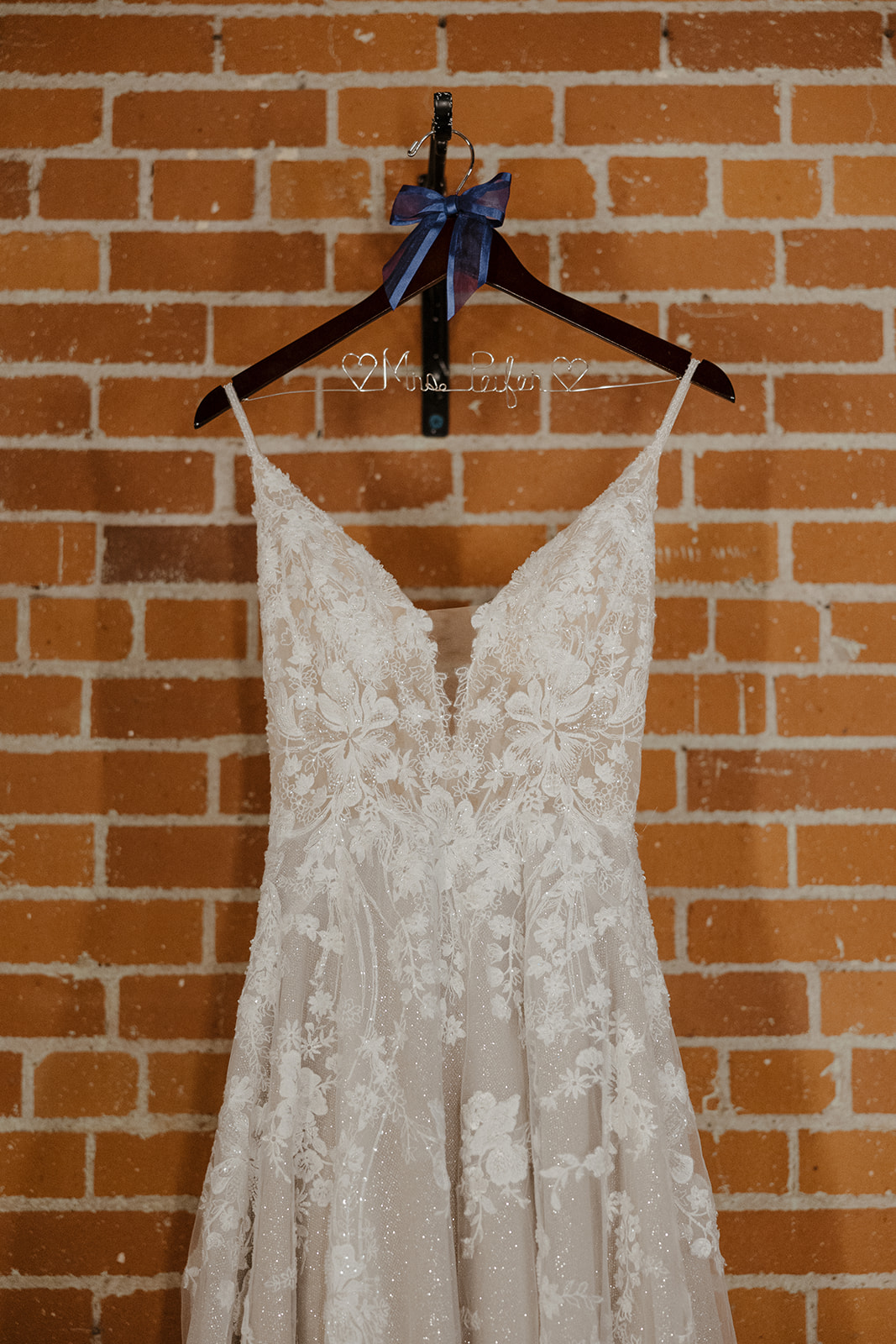 Stunning wedding dress hangs in front of a brick wall before the dreamy Arizona wedding day