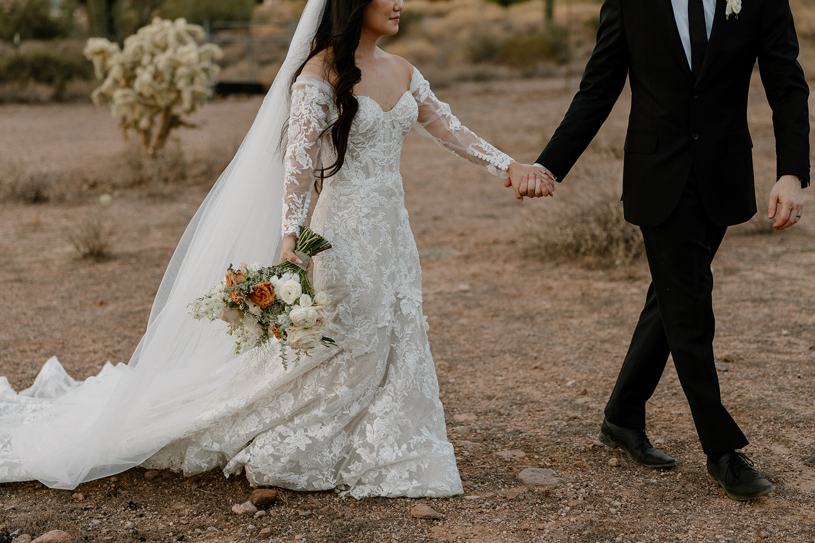 bride and groom walk together hand in hand through the desert