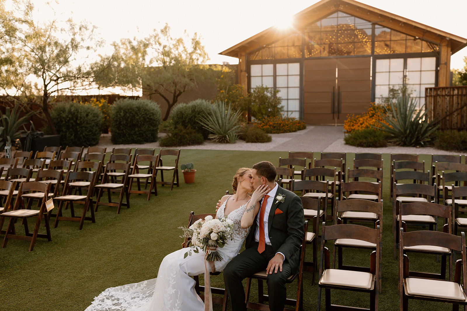 bride and groom share a kiss in front of the stunning Arizona desert wedding venue in the background