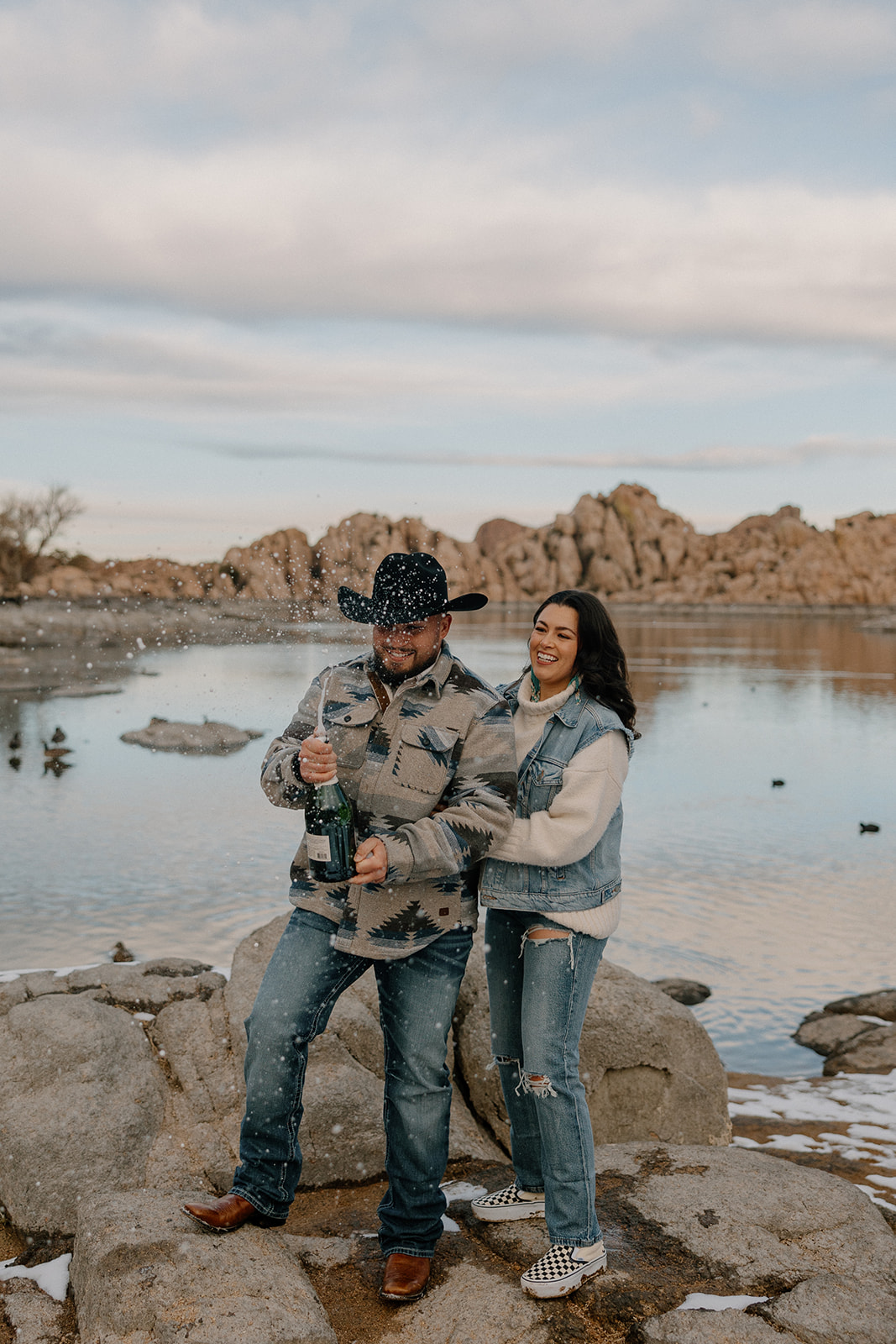 Couple pop champagne on the lakeshore during their Arizona lake engagement photos