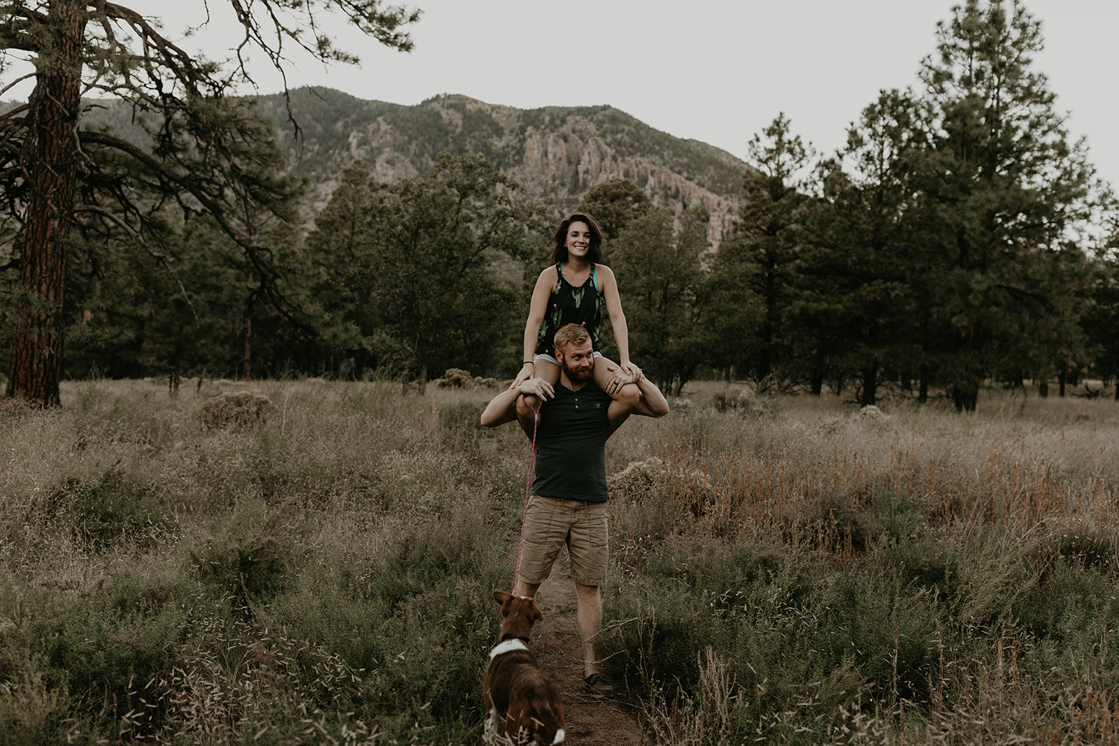 couple pose with their dog in a field outside their house, this photo is a great couple photoshoot ideas at home