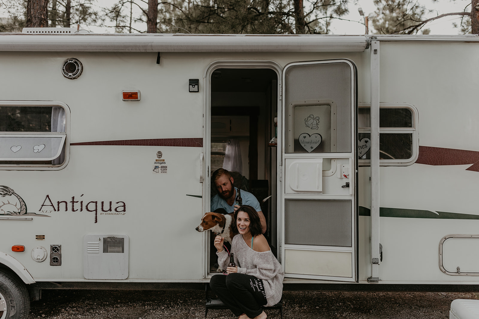 husband and wife pose with their dog at the door to their home