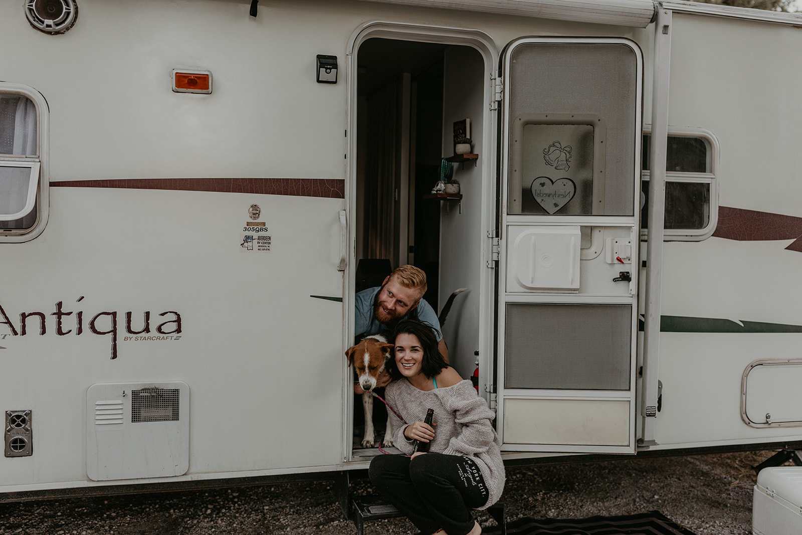 husband and wife pose with their dog at the door to their home