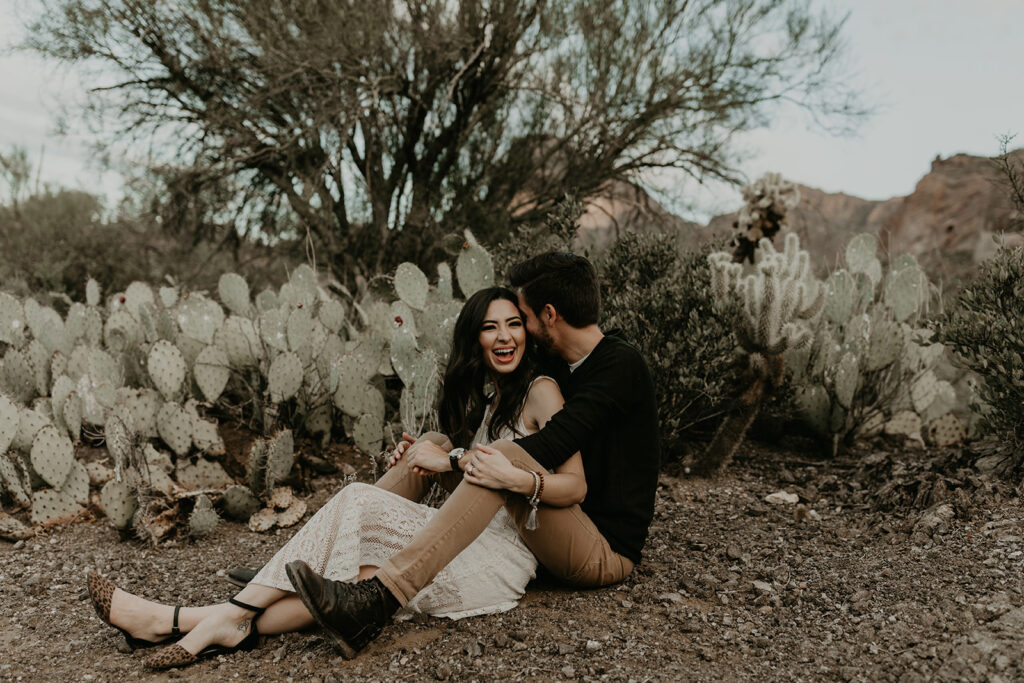 stunning couple sit in the Arizona desert with cactus in the background