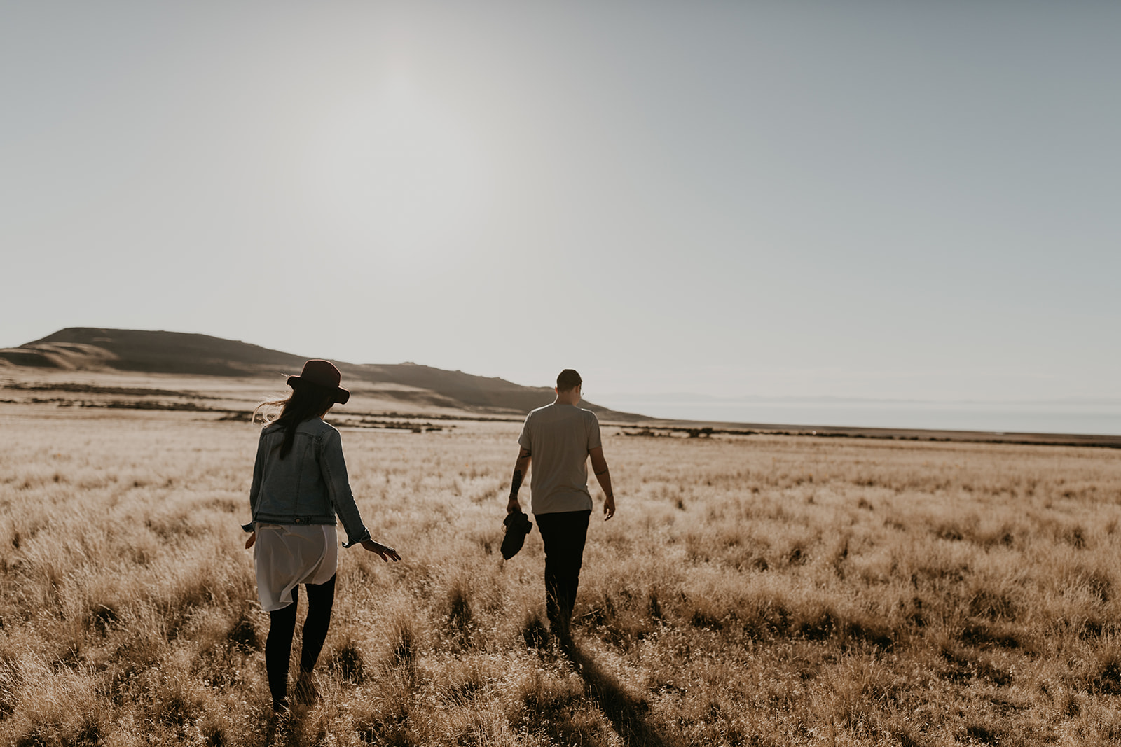 couple walk through a prairie with a hill in the background 