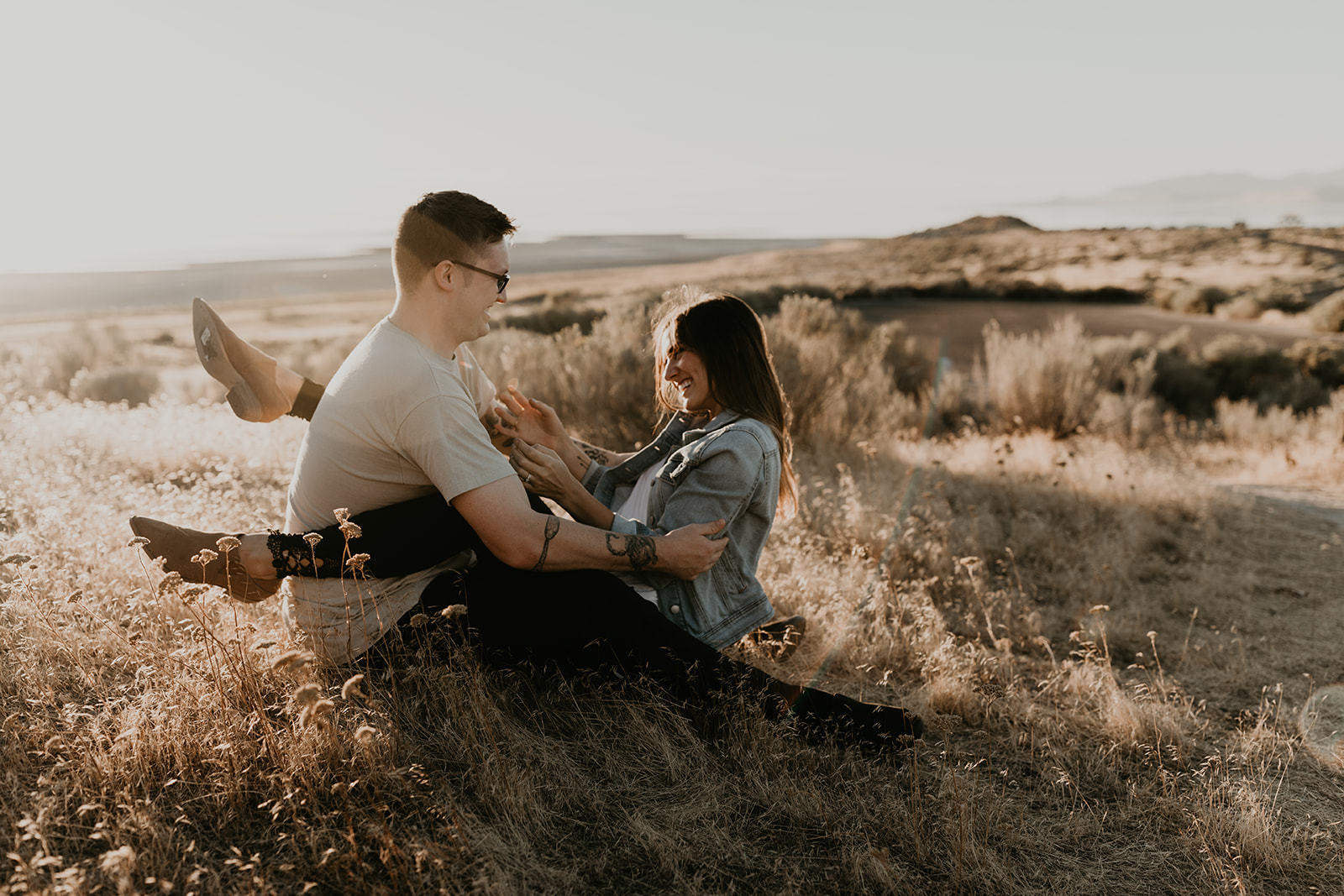 couple sit together in a prairie field during their Engagement photos in Utah