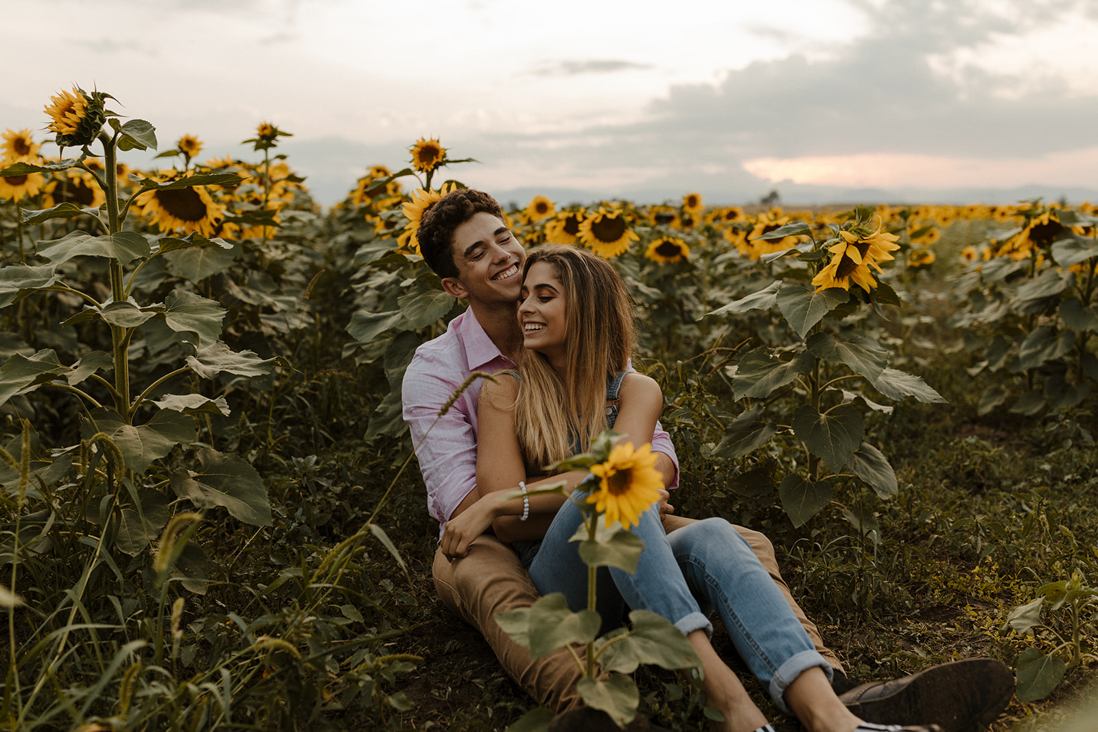 beautiful couple sit together during their Denver sunflower field engagement photos