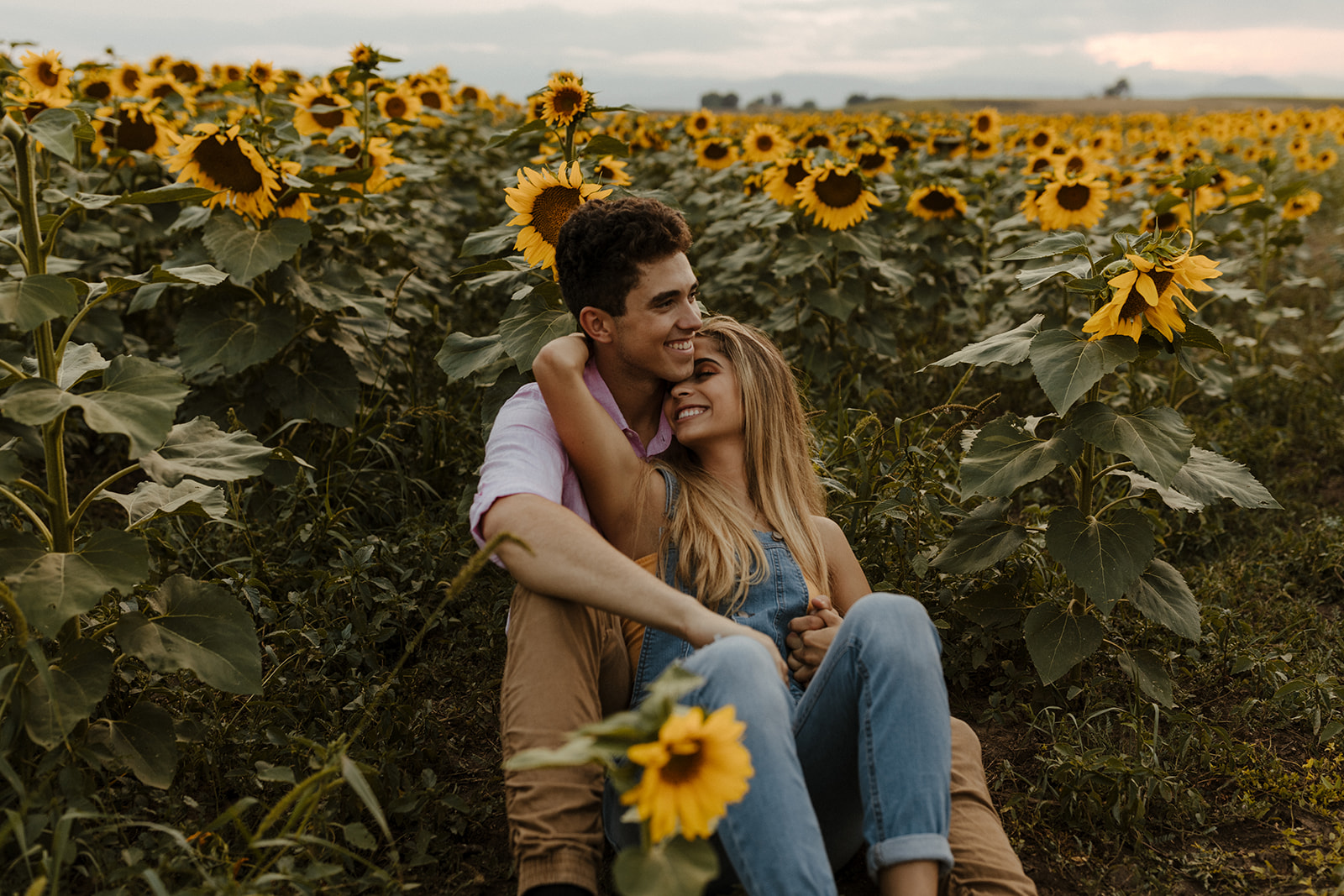 beautiful couple sit together during their Denver sunflower field engagement photos