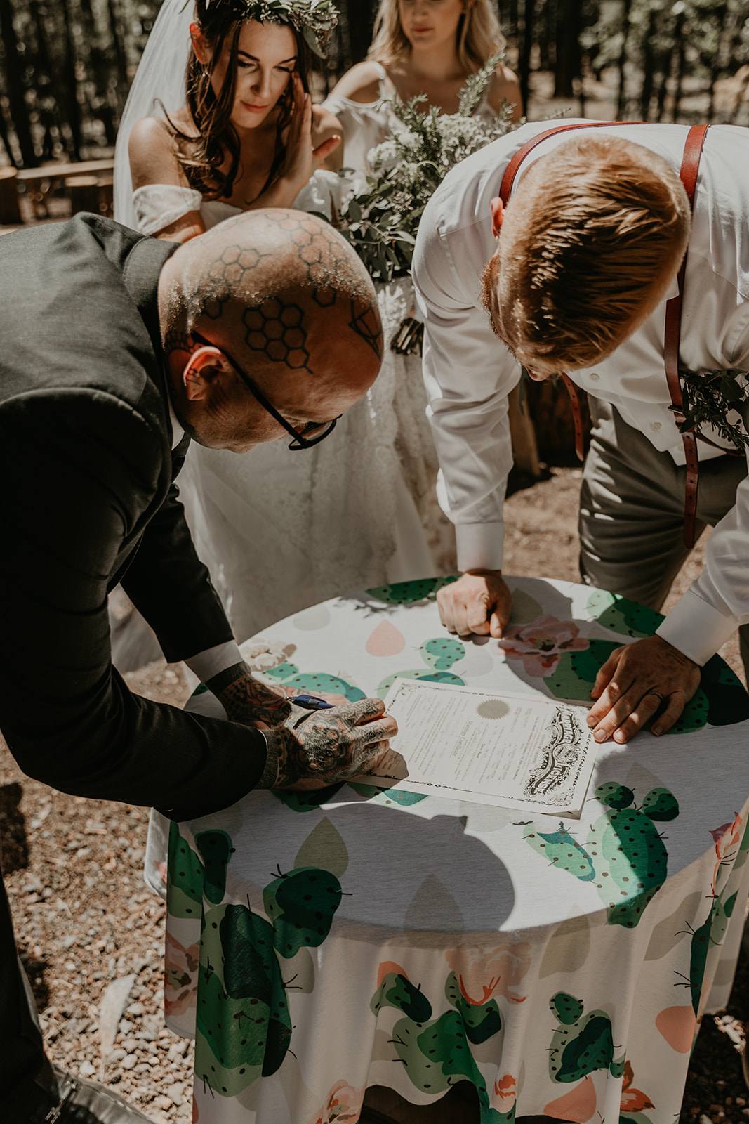 bride and groom look on as the officiant signs there marriage certificate 