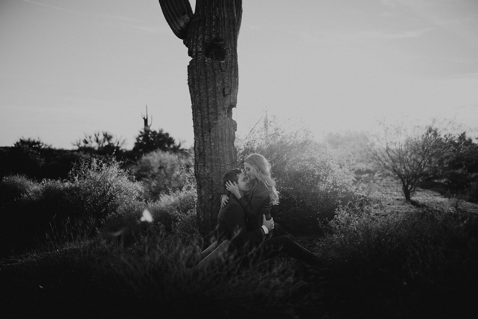 couple pose beside the cactus during their desert engagement photoshoot