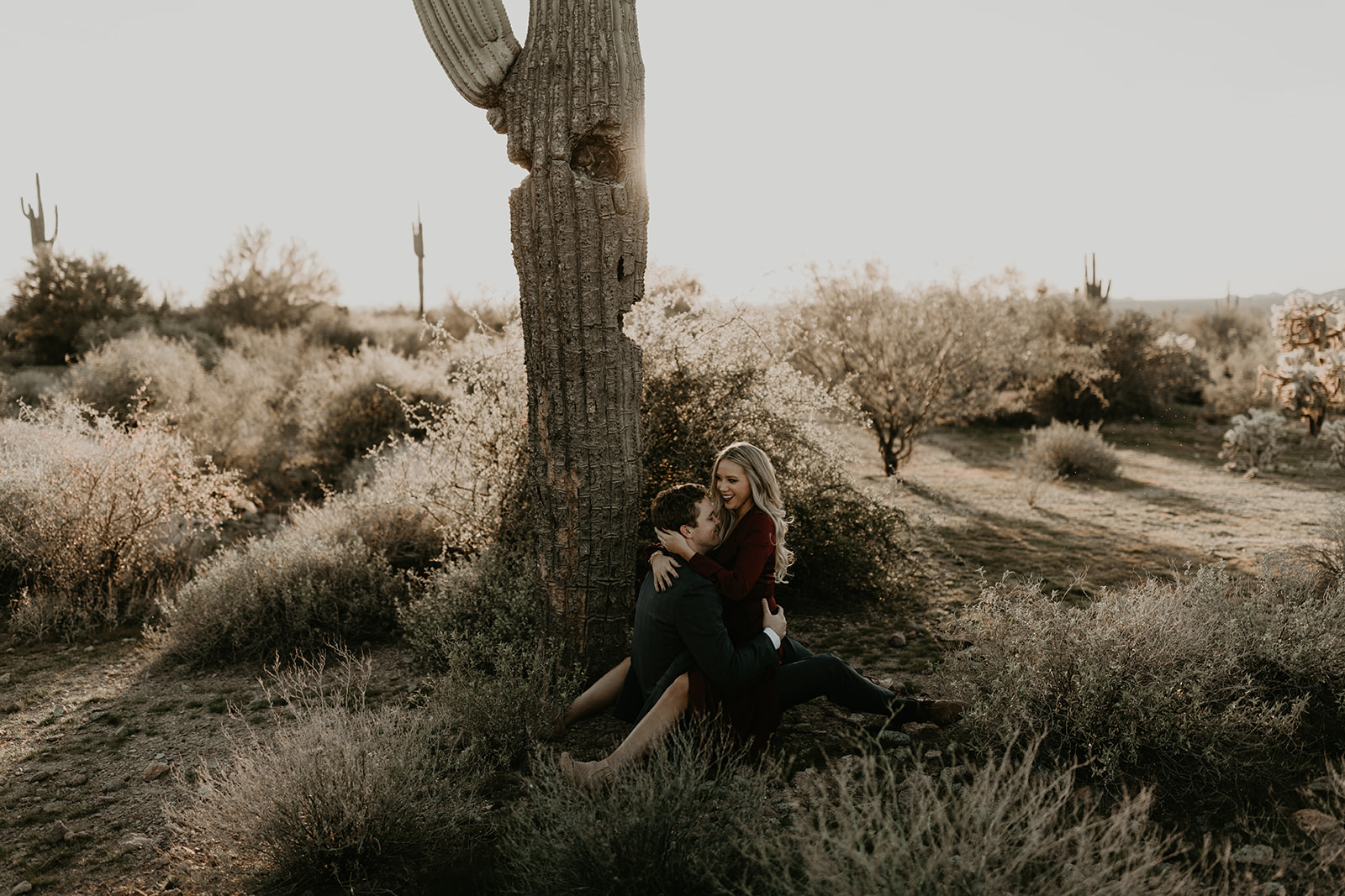 couple pose beside the cactus during their desert engagement photoshoot