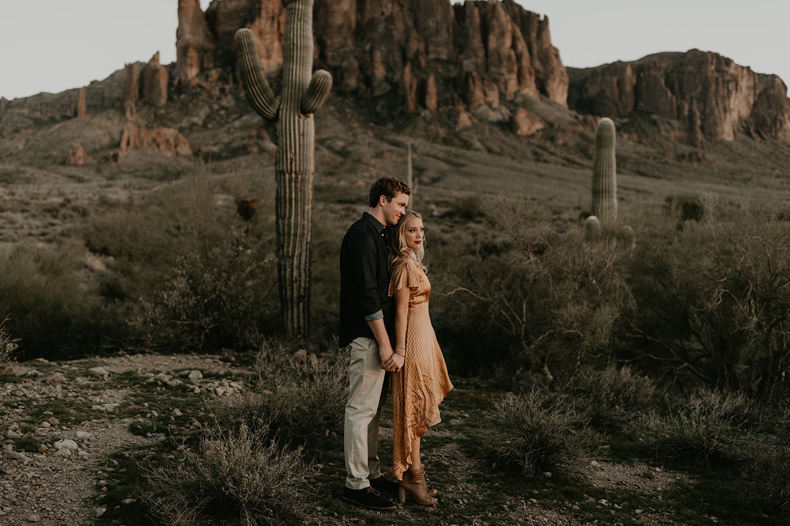 couple pose beside the cactus during their desert engagement photoshoot