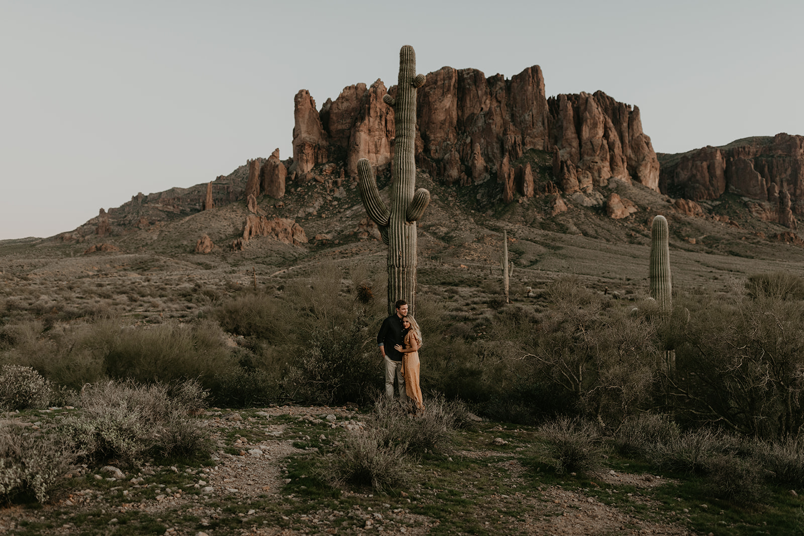 couple pose beside the cactus during their desert engagement photoshoot