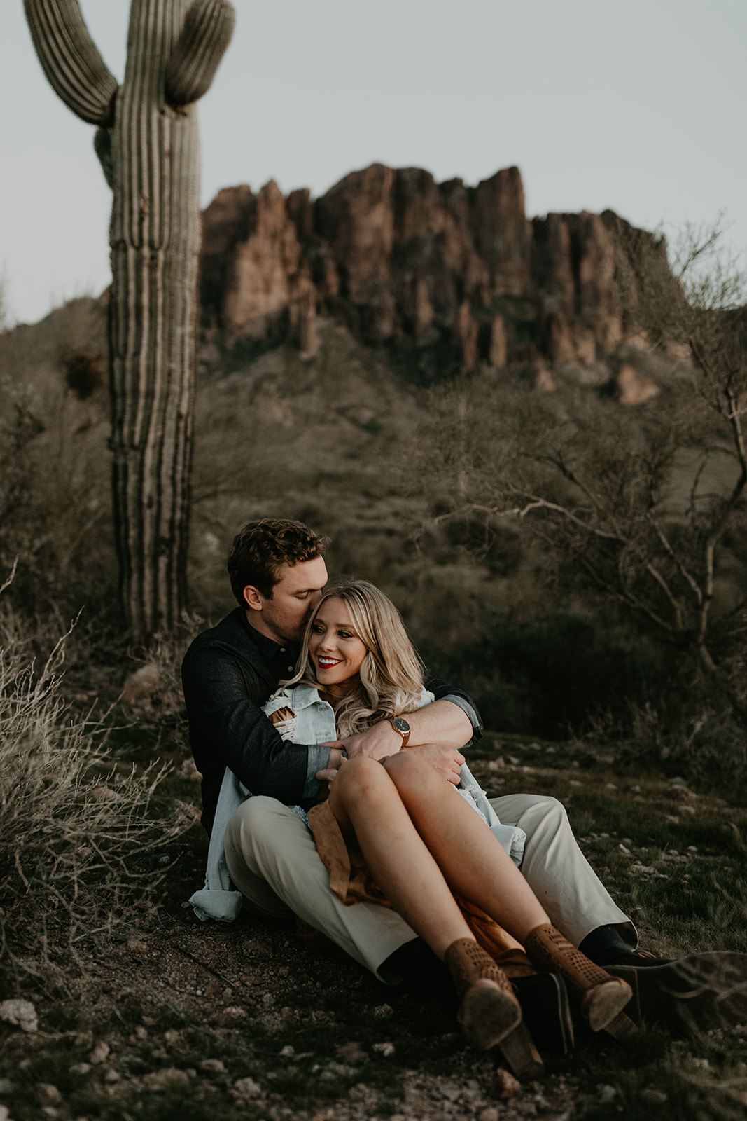 couple pose beside the cactus during their desert engagement photoshoot