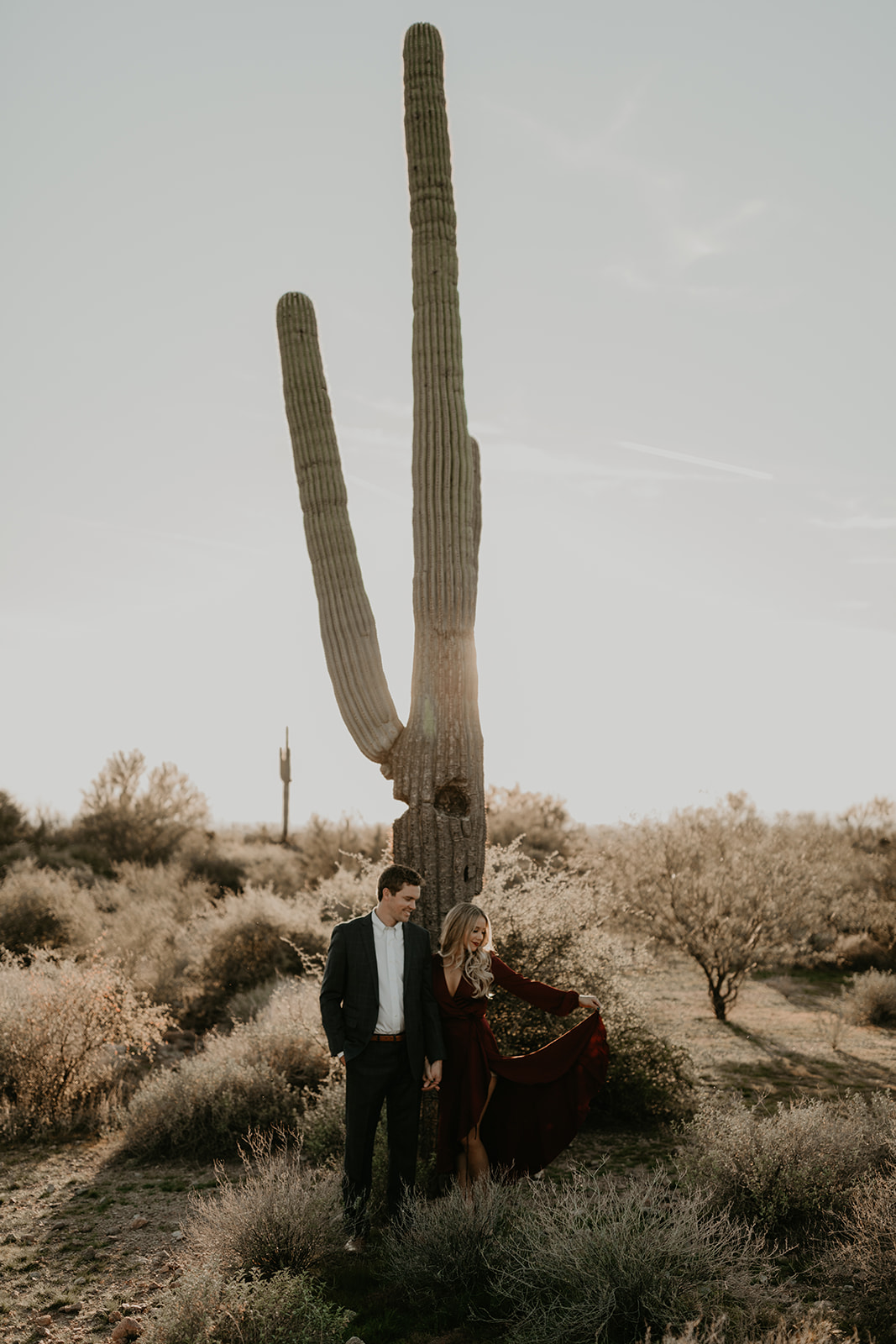 couple pose beside the cactus during their desert engagement photoshoot