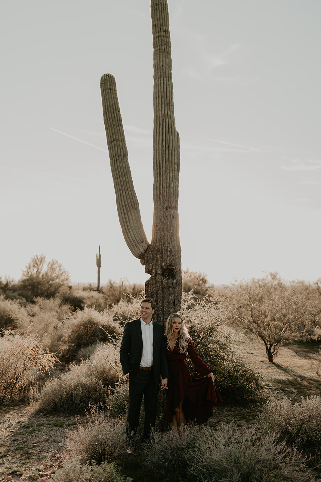 couple pose beside the cactus during their desert engagement photoshoot