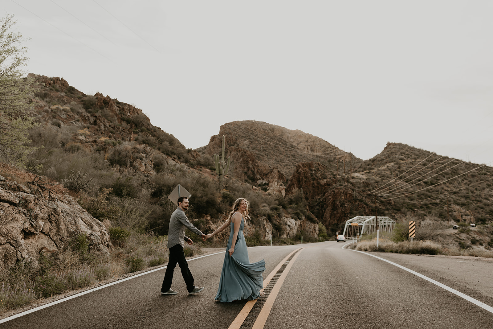 couple pose walking across the road in Arizona during their engagement photoshoot