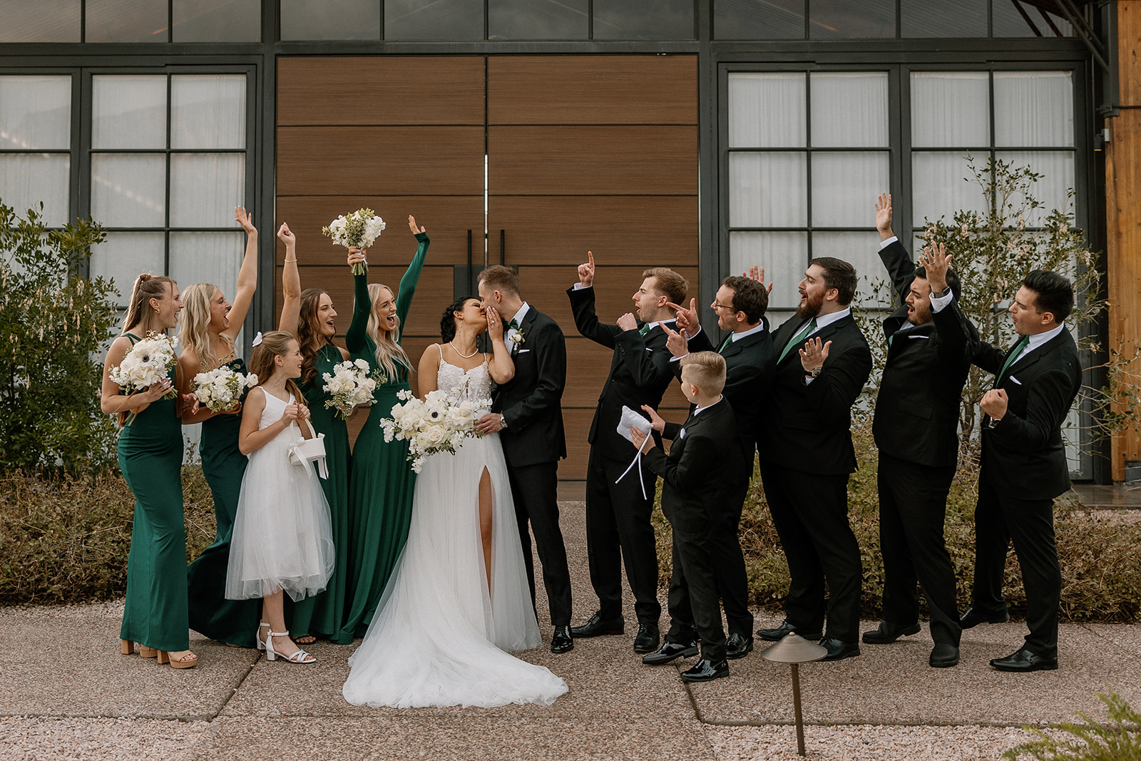 bride and groom share a kiss while the wedding party celebrates