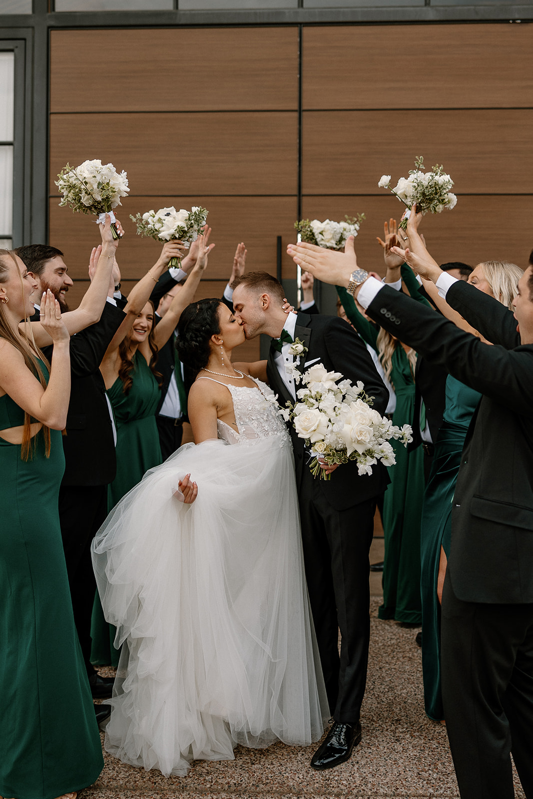 bride and groom share a kiss while the wedding party celebrates