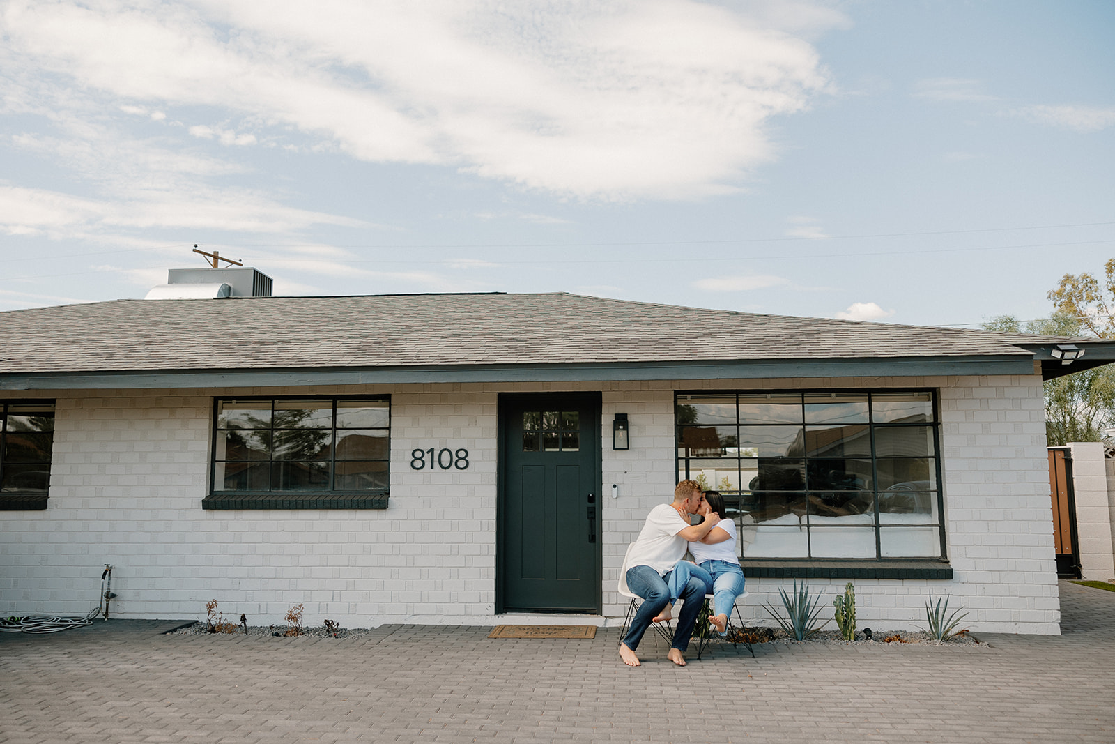 couple sits outside their home, the scene for their At home engagement photoshoot