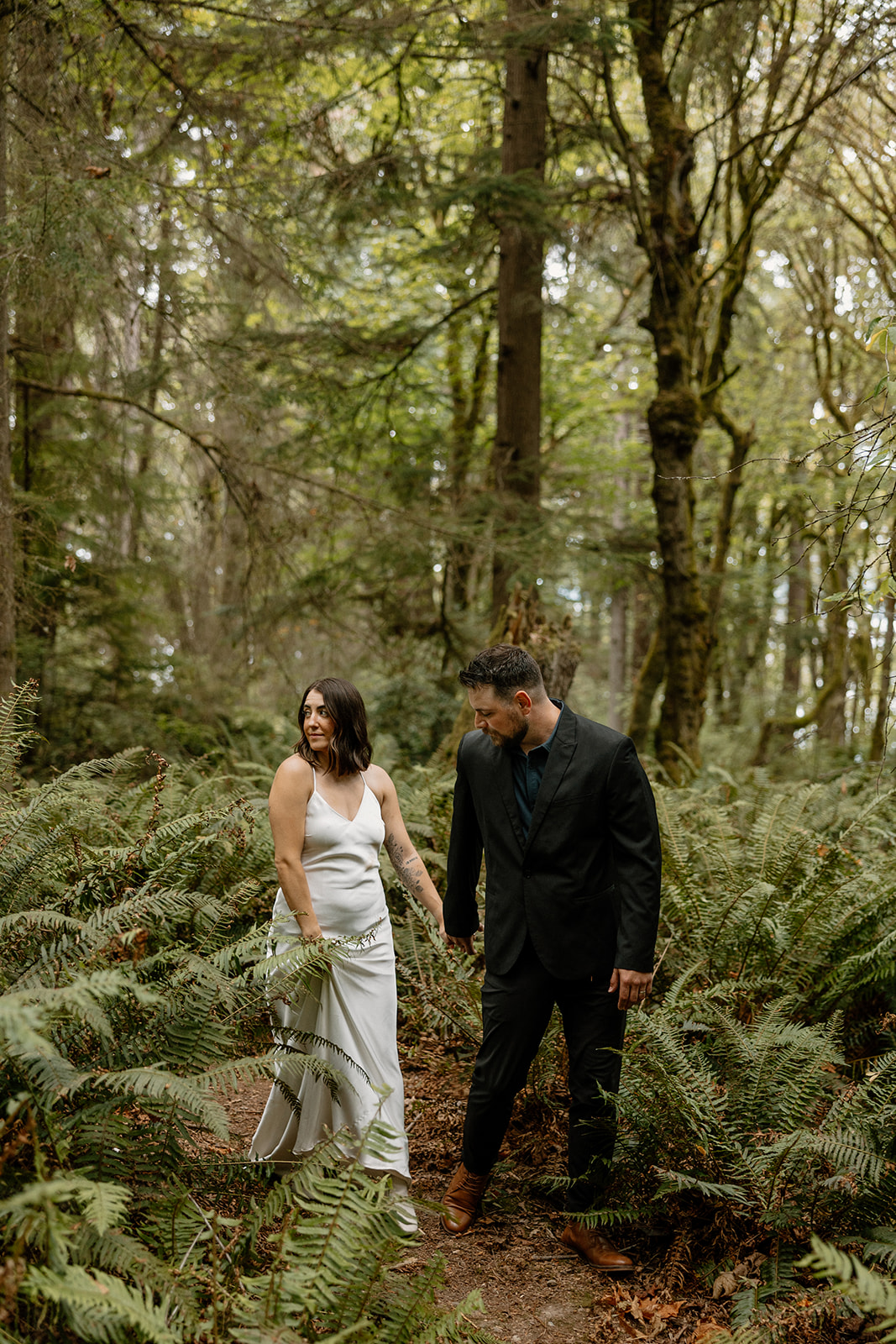 beautiful couple walk through the forest together during their PNW forest wedding anniversary photoshoot