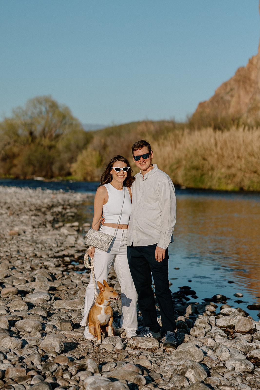 beautiful couple pose with their dog beside a river