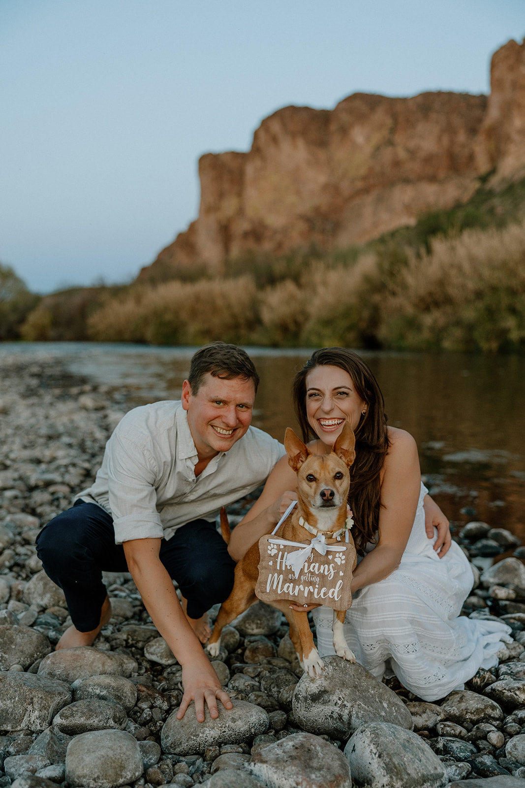 couple poses by the water with their dog