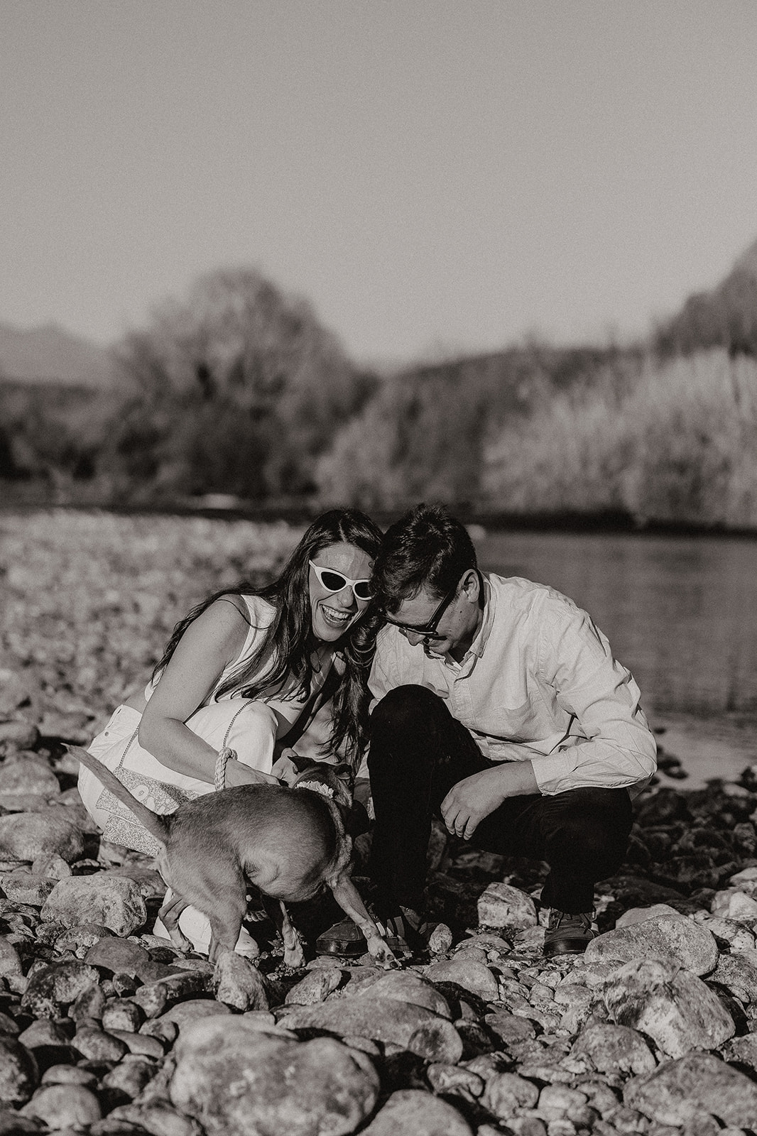 beautiful couple pose with their dog beside a river