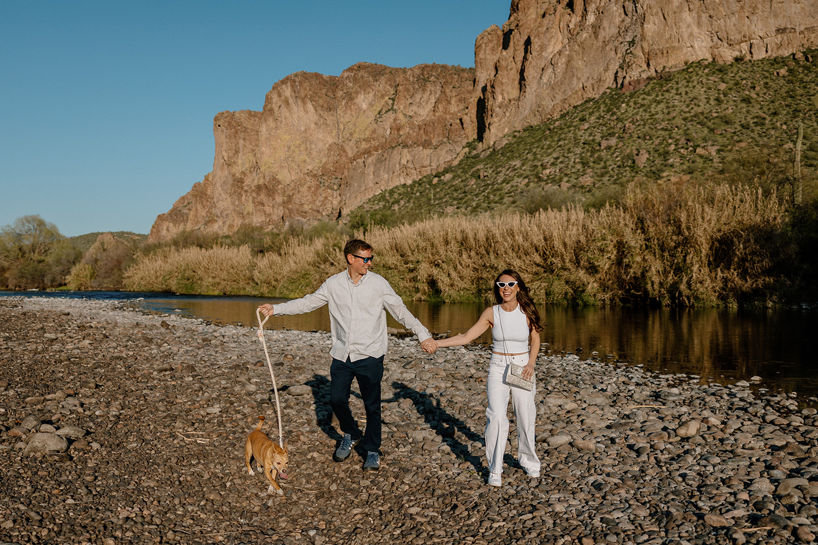 beautiful couple pose with their dog beside a river