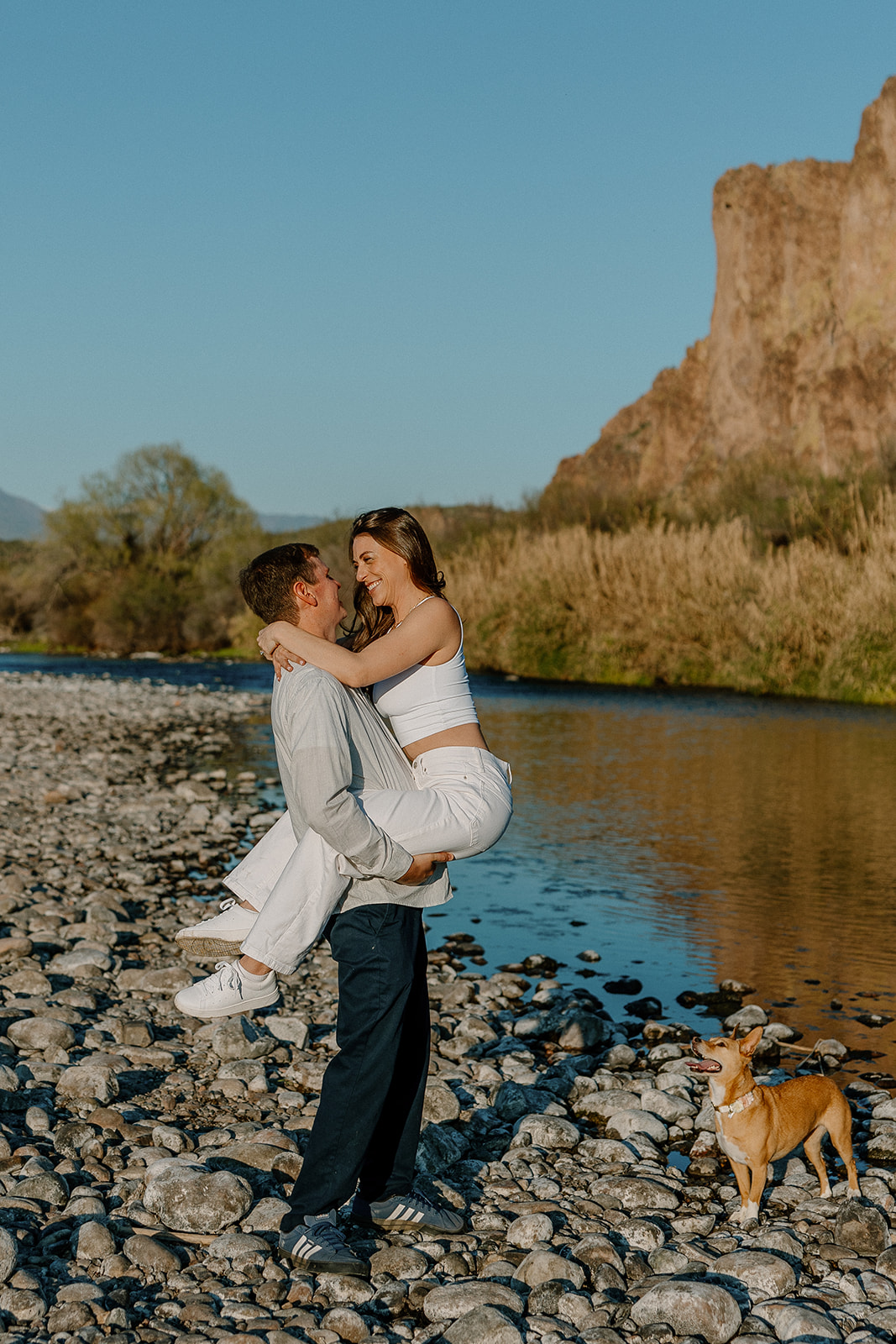 beautiful couple pose with their dog beside a river