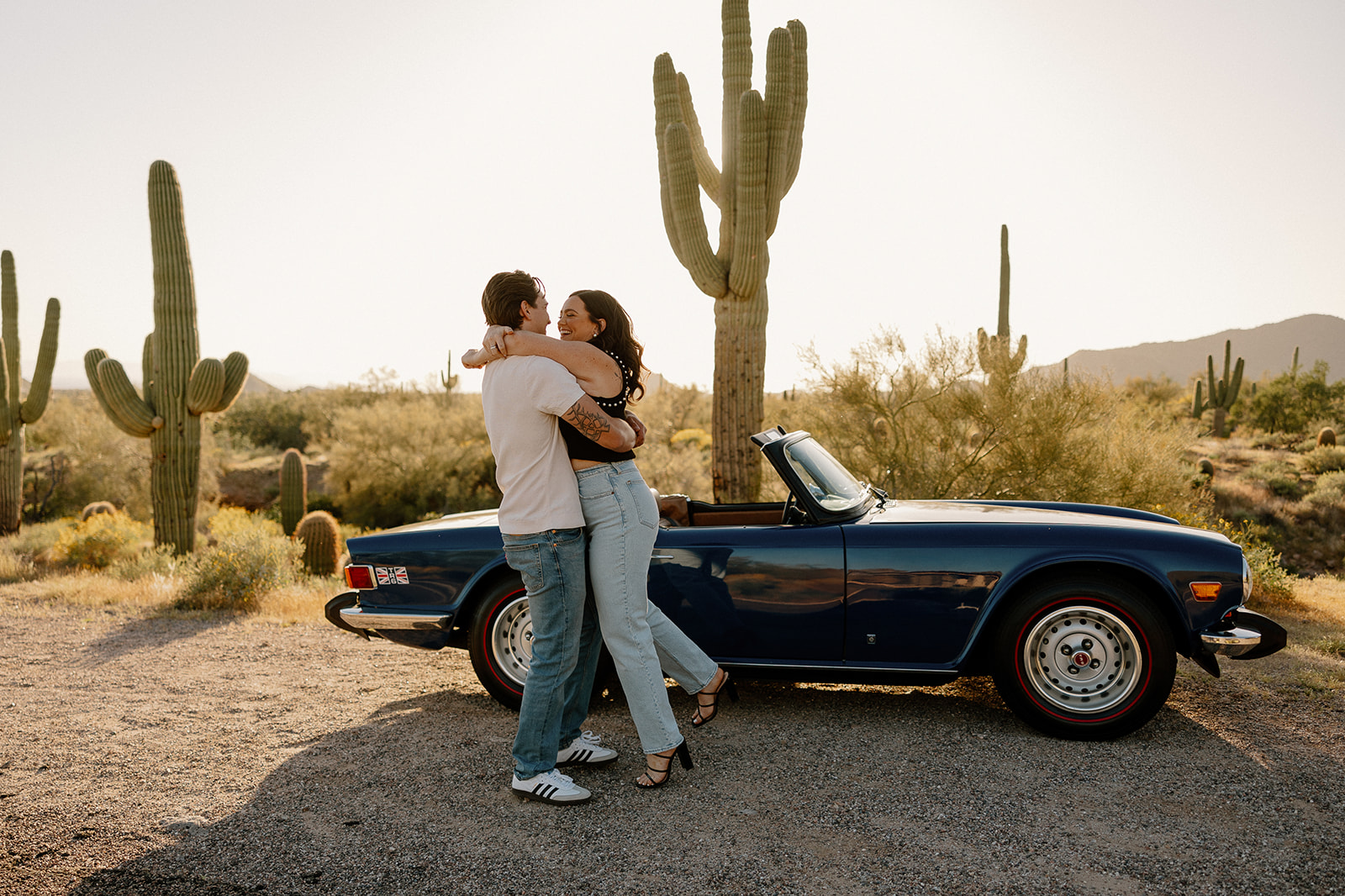 stunning couple pose with a vintage car during their engagement photos in the Arizona dessert