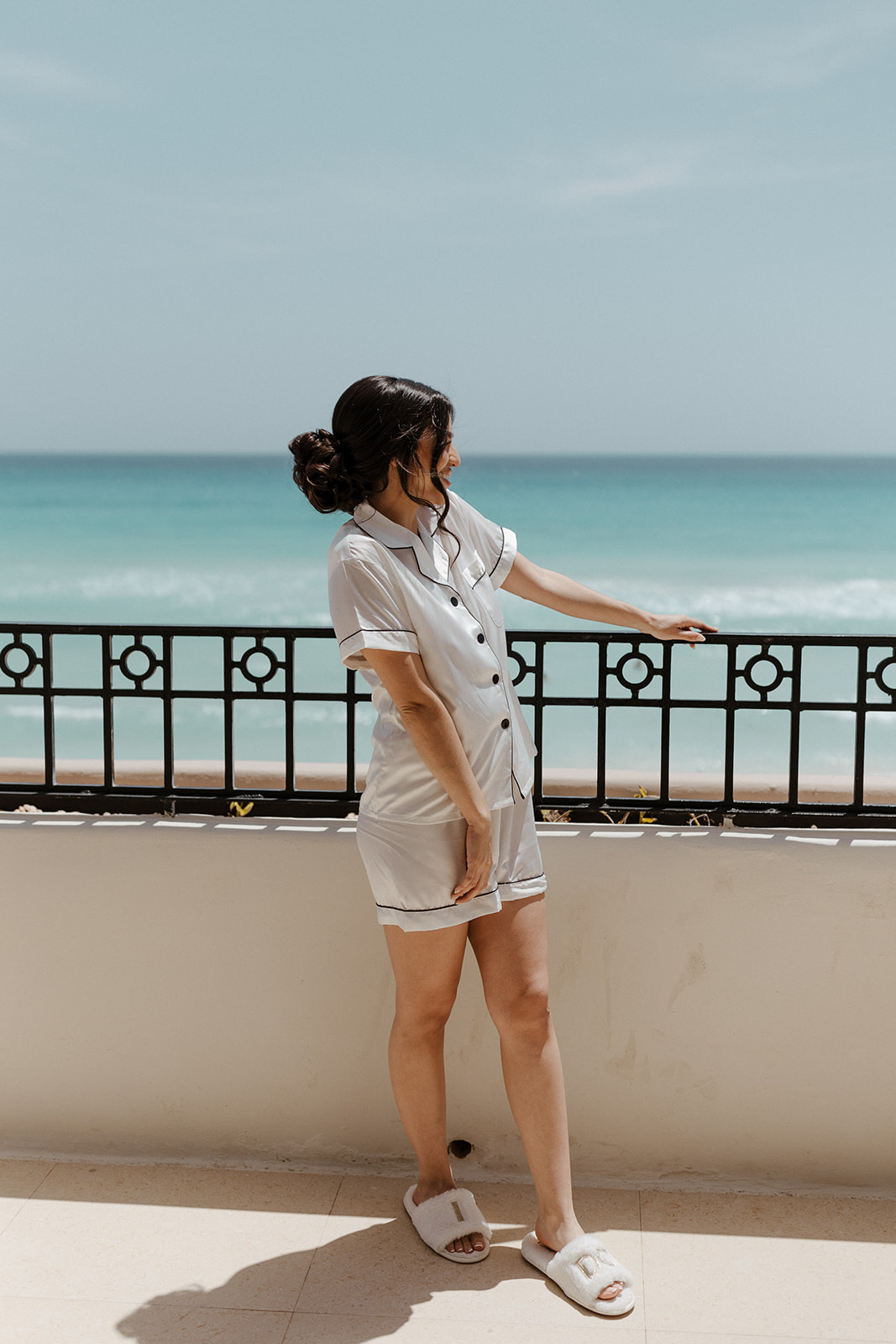 The bride overlooks the ocean on the patio while getting ready for her destination wedding, wearing a silky pajama set that is as soft as the clouds.