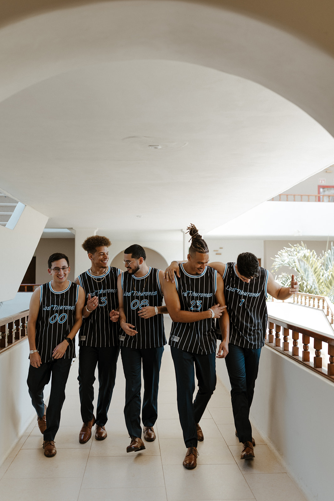 groomsmen pose in basketball jerseys that are black with blue stripes during destination wedding