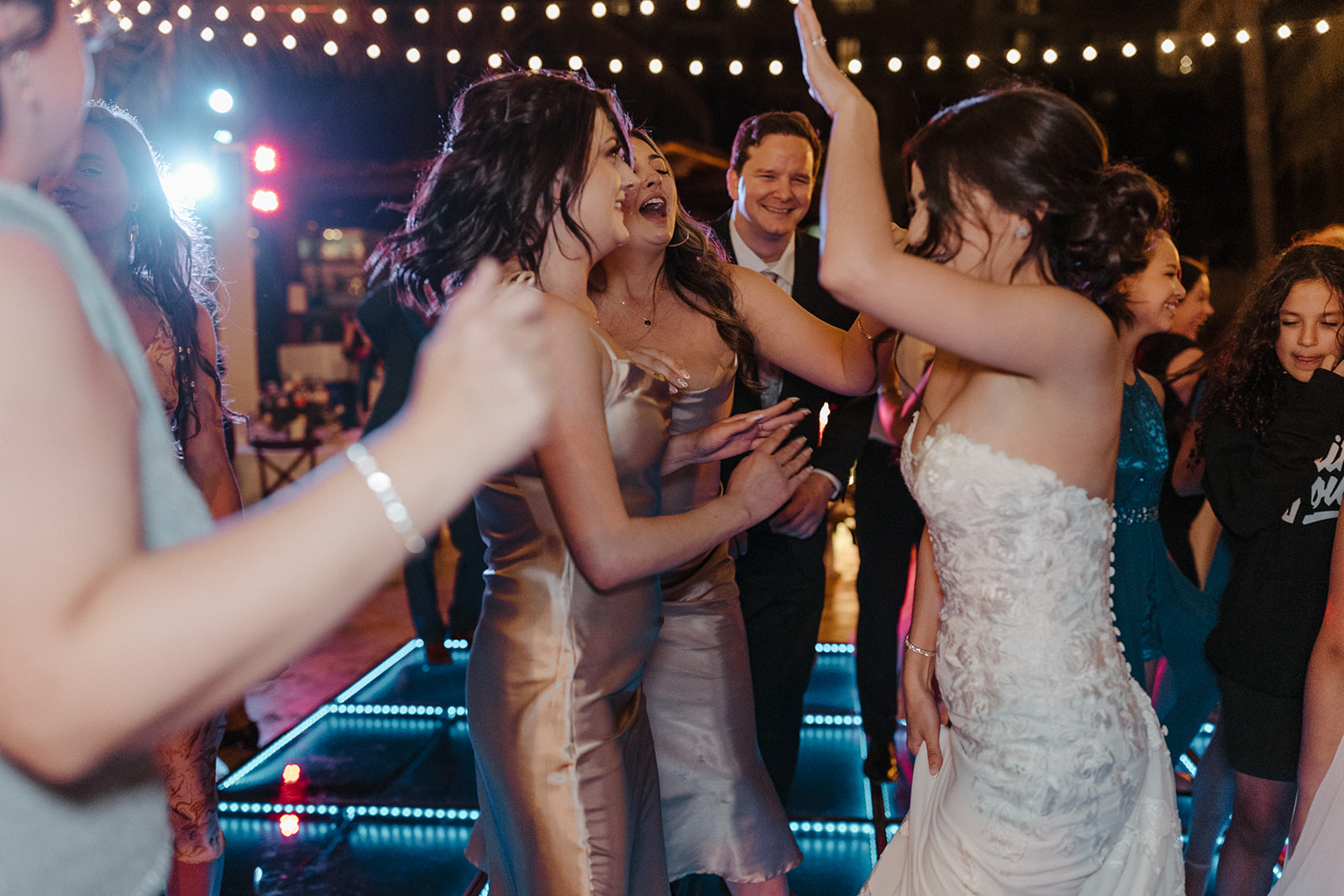 bride in white lacy dress dancing with bridesmaids in chrome dresses