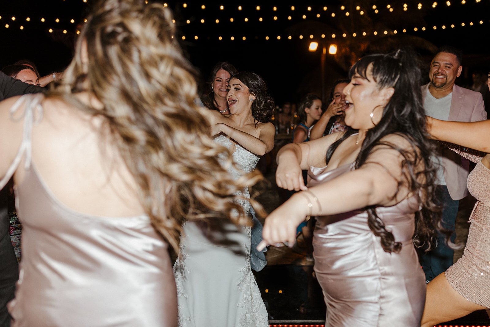 bride in white lacy dress dancing with bridesmaids in chrome dresses