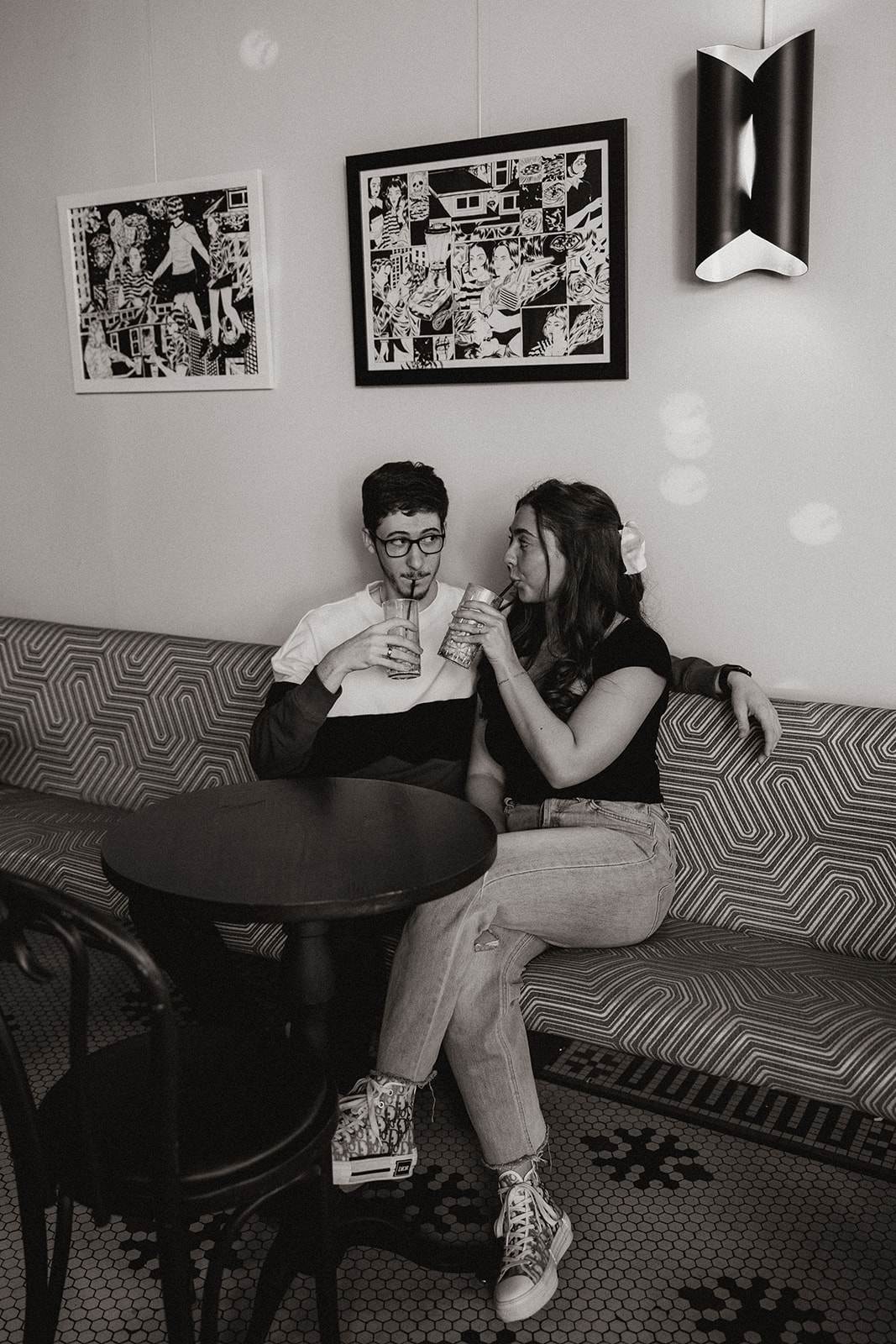 couple sits on a red and white bench while sipping an iced coffee together