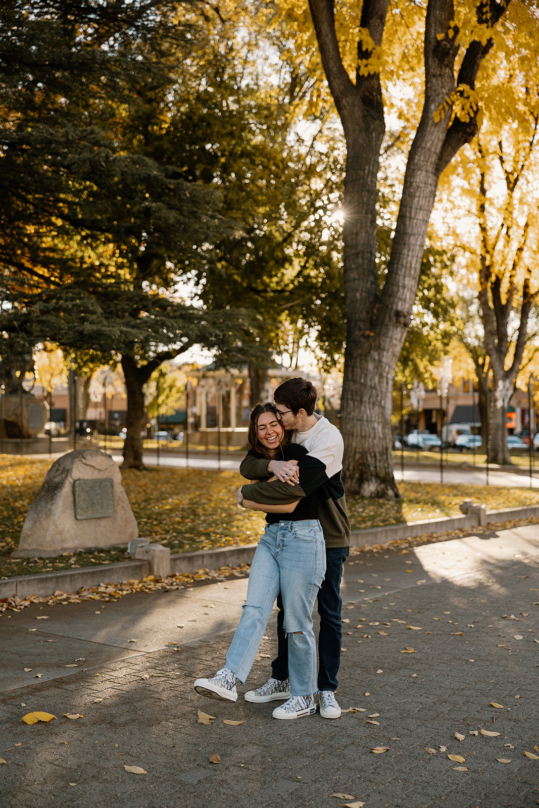 couple holding each other during the fall season with orange and yellow leaves on the ground