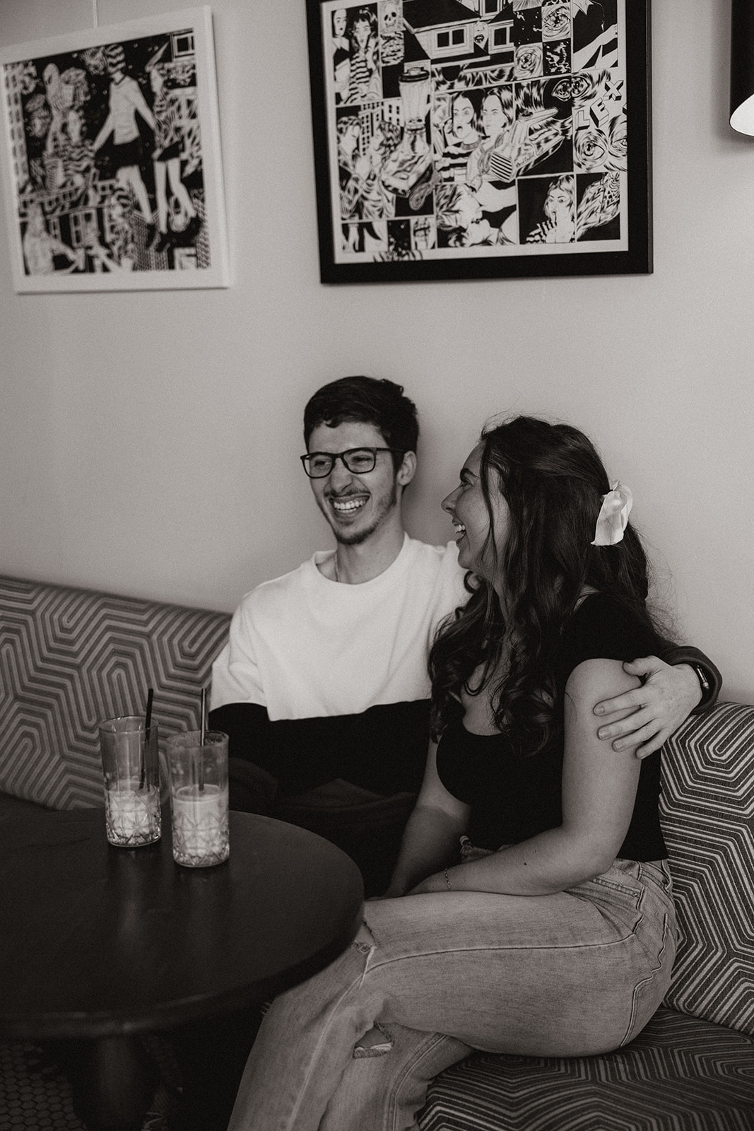 couple sits on a red and white bench while sipping an iced coffee together