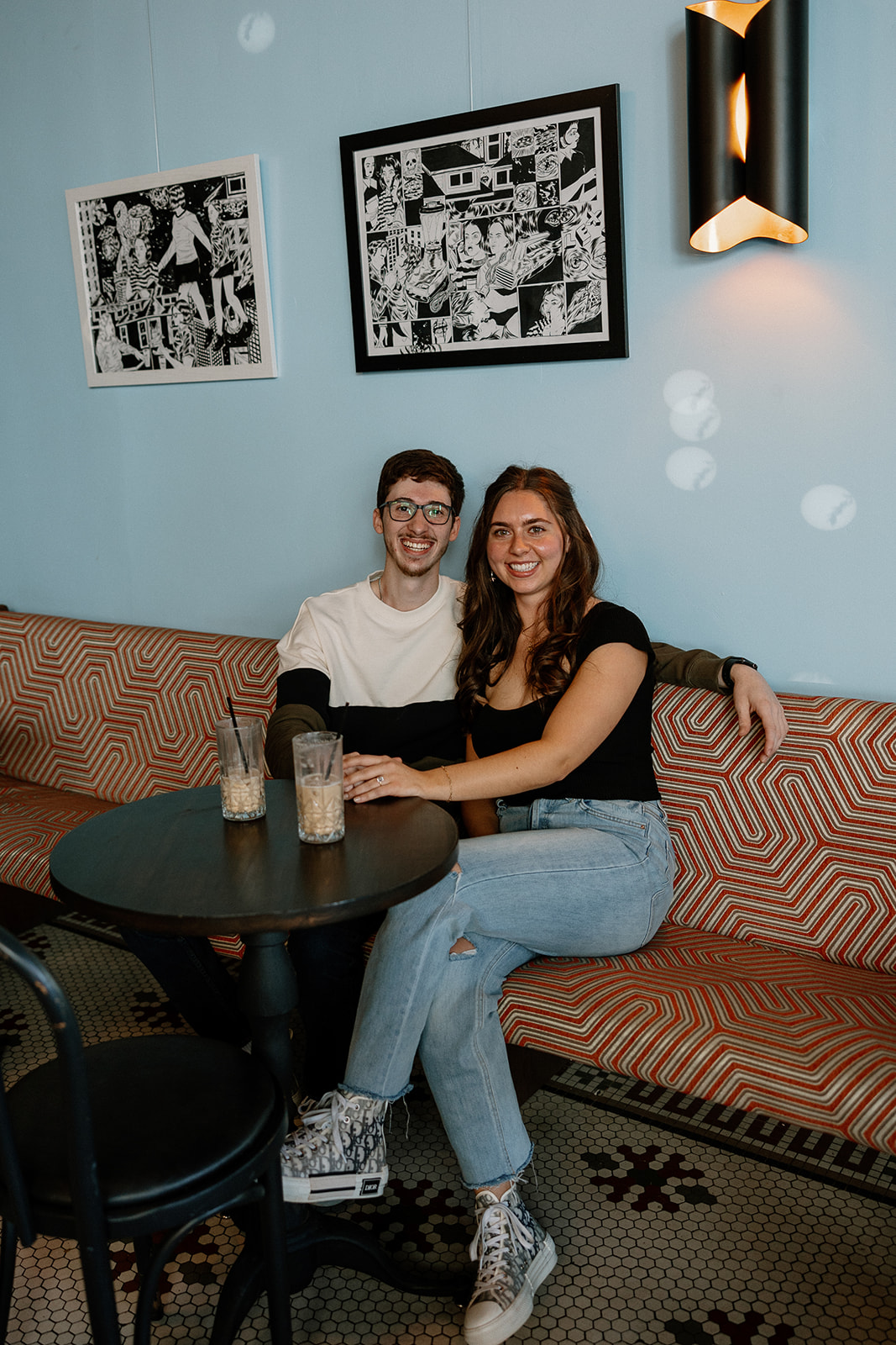 couple sits on a red and white bench while sipping an iced coffee together