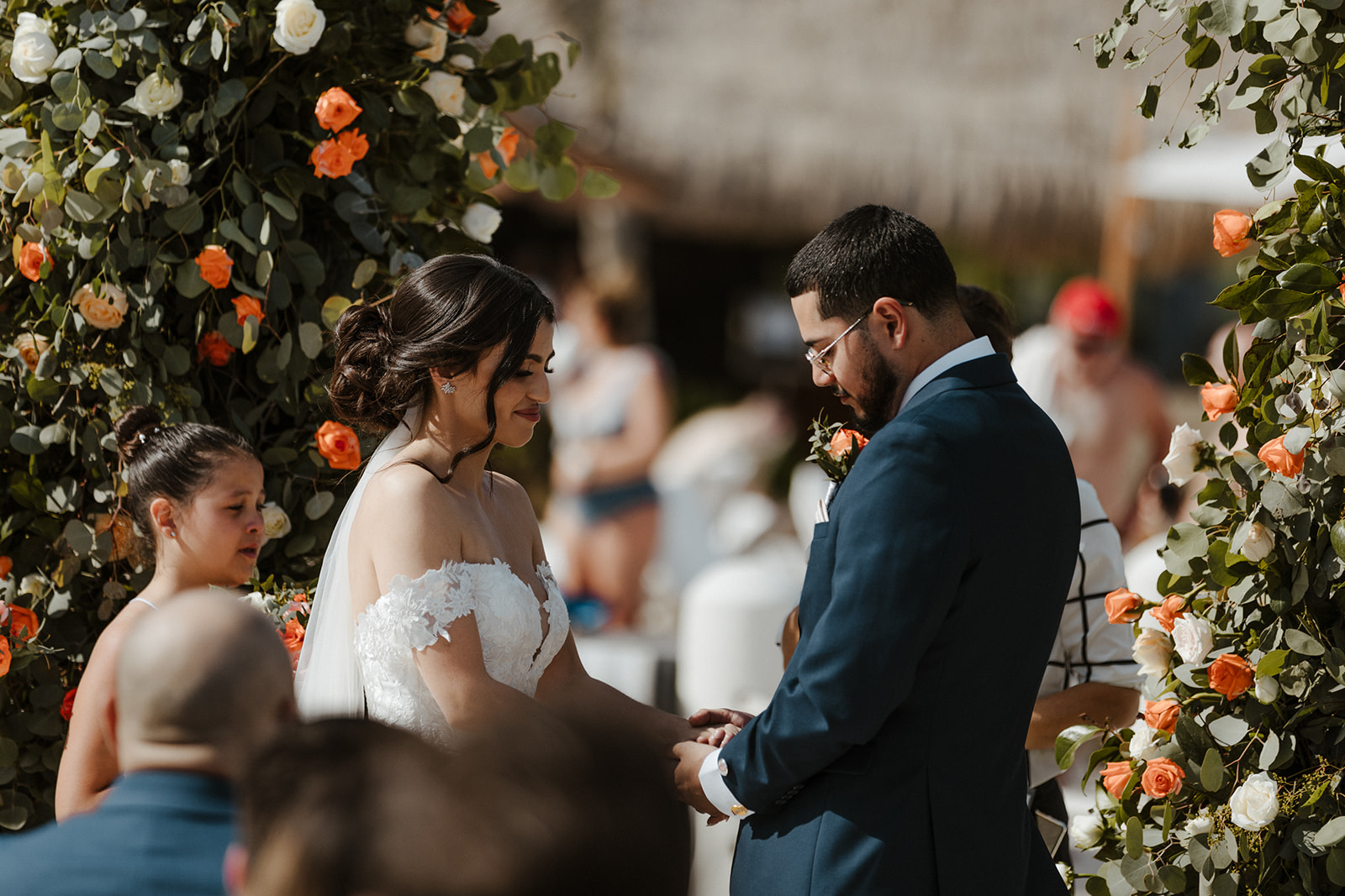 bride and groom pose during their destination wedding in cabo surrounded by pink, orange, and white flowers and their loved ones