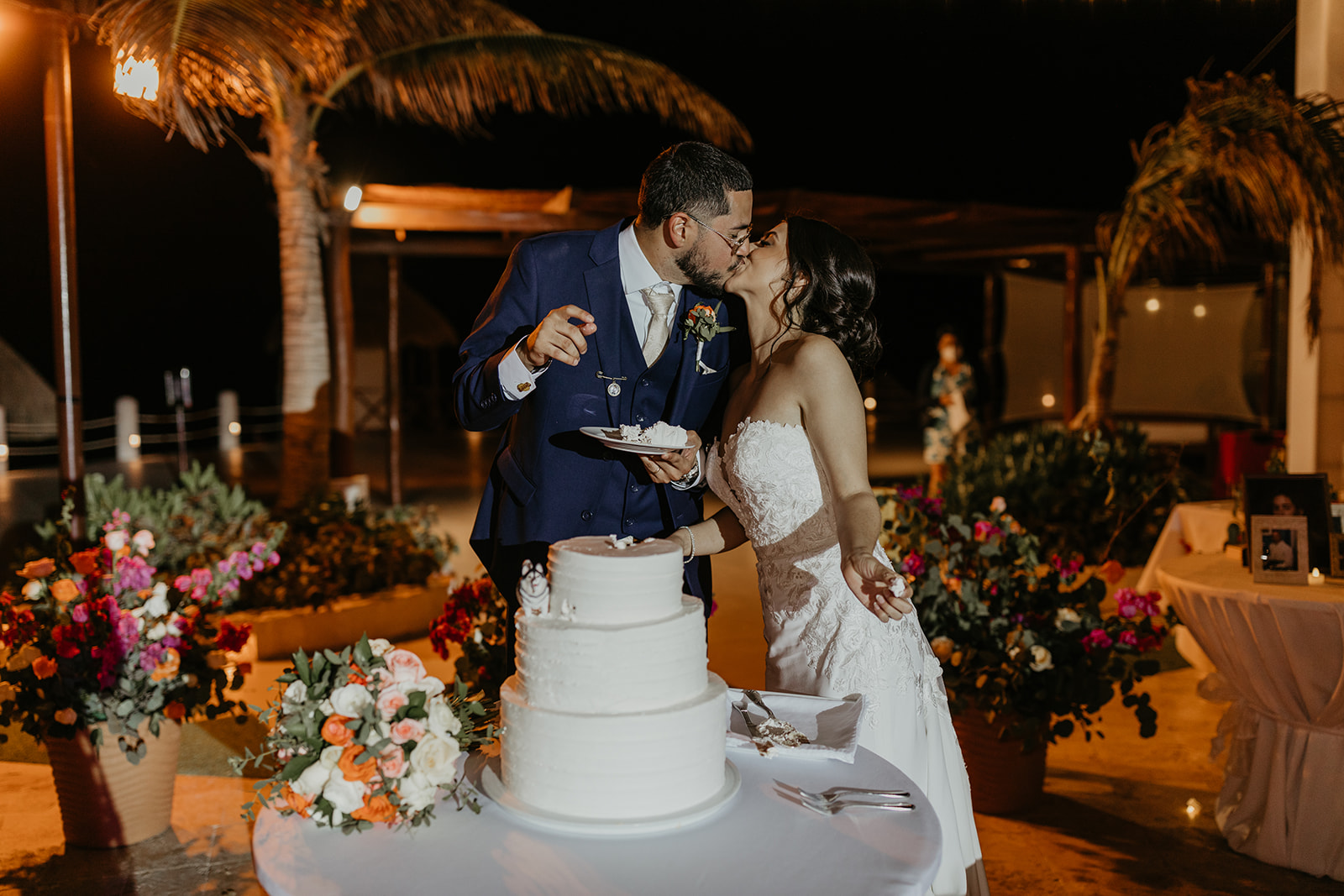 bride and groom share a kiss during their cake cutting ceremony surrounded by orange, pink, and white flowers