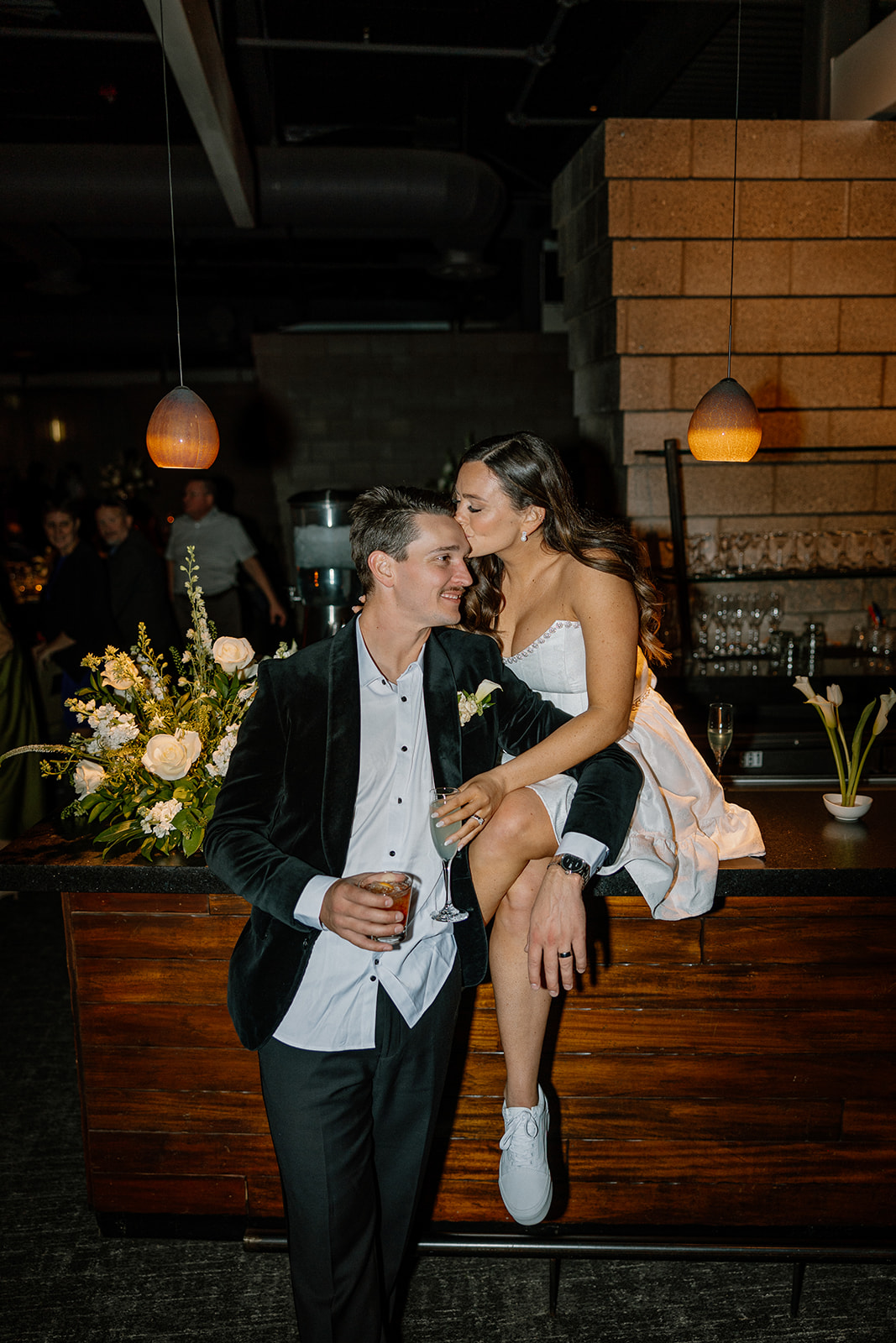 bride on bar in short white dress kissing groom on cheek 