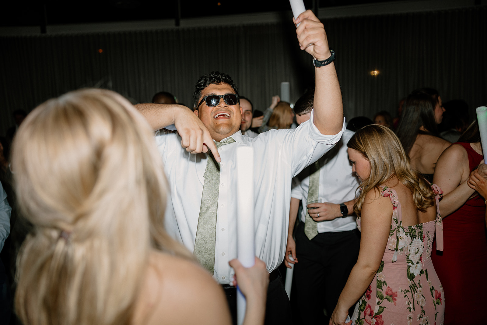 wedding guest dancing with hands in the air while wearing sunglasses