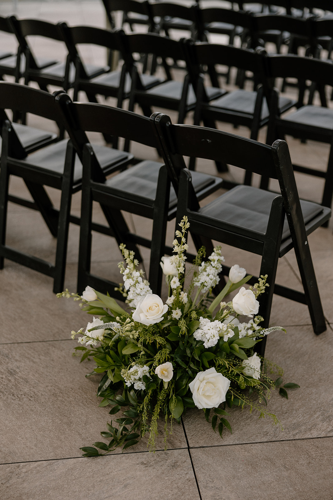 white and green flower arrangement on ground behind black wooden chairs