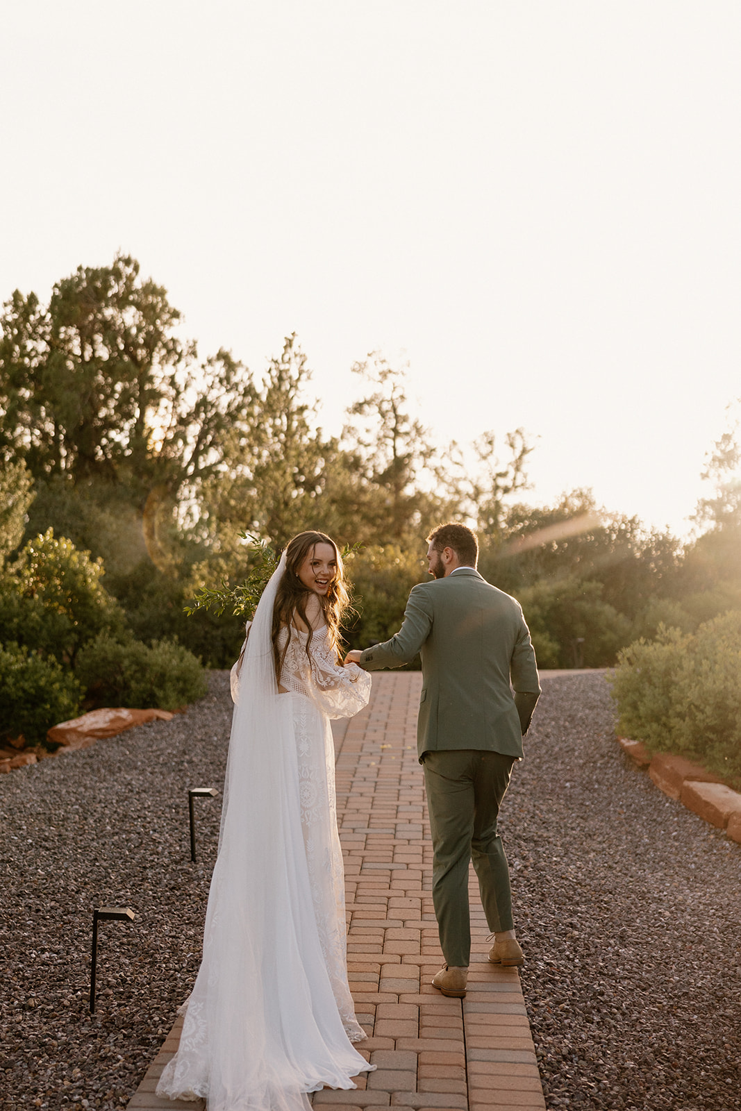 Groom holding bride's hand and leading her into distance as bride looks back laughing